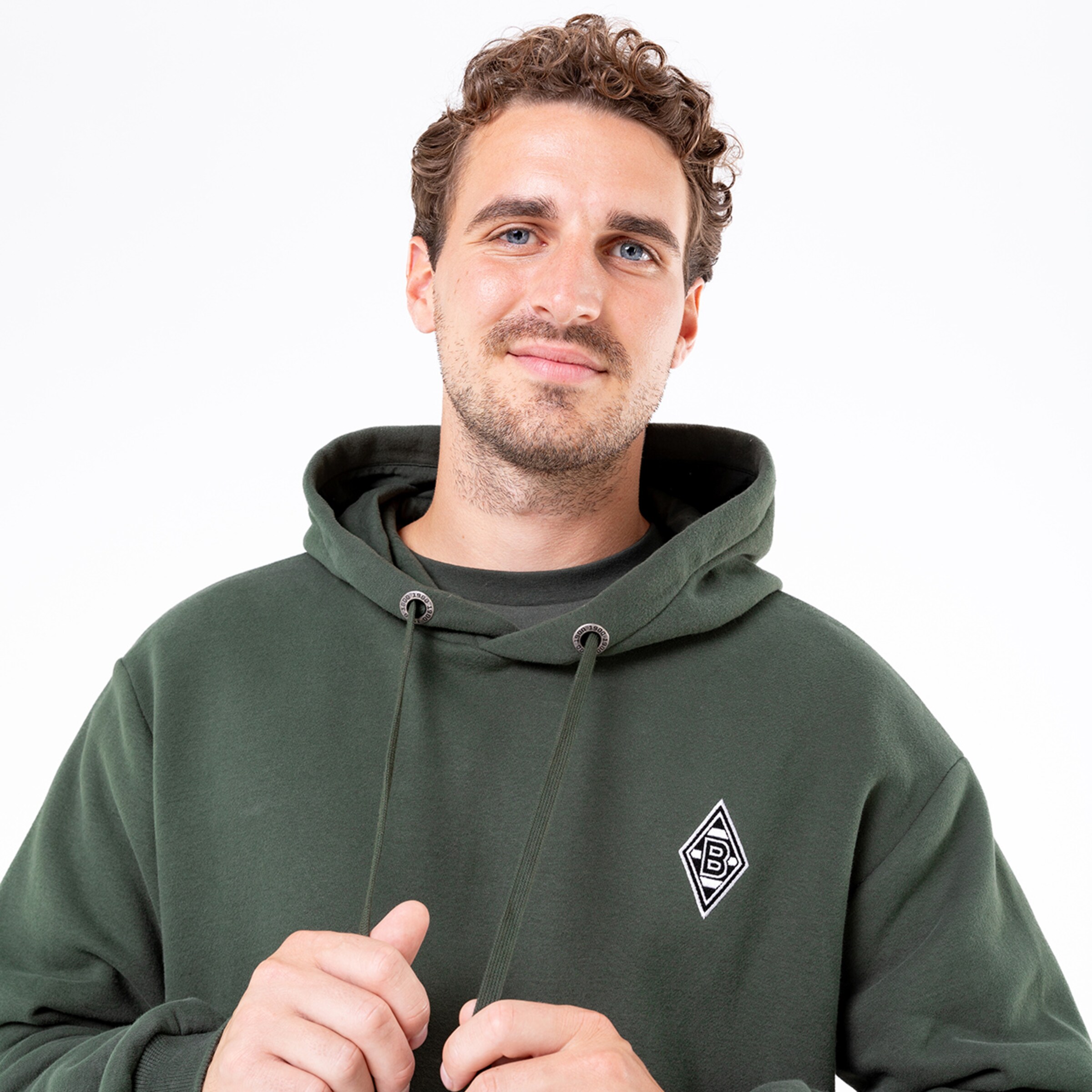 Mann in grünem Hoodie mit Logo lächelt in die Kamera.