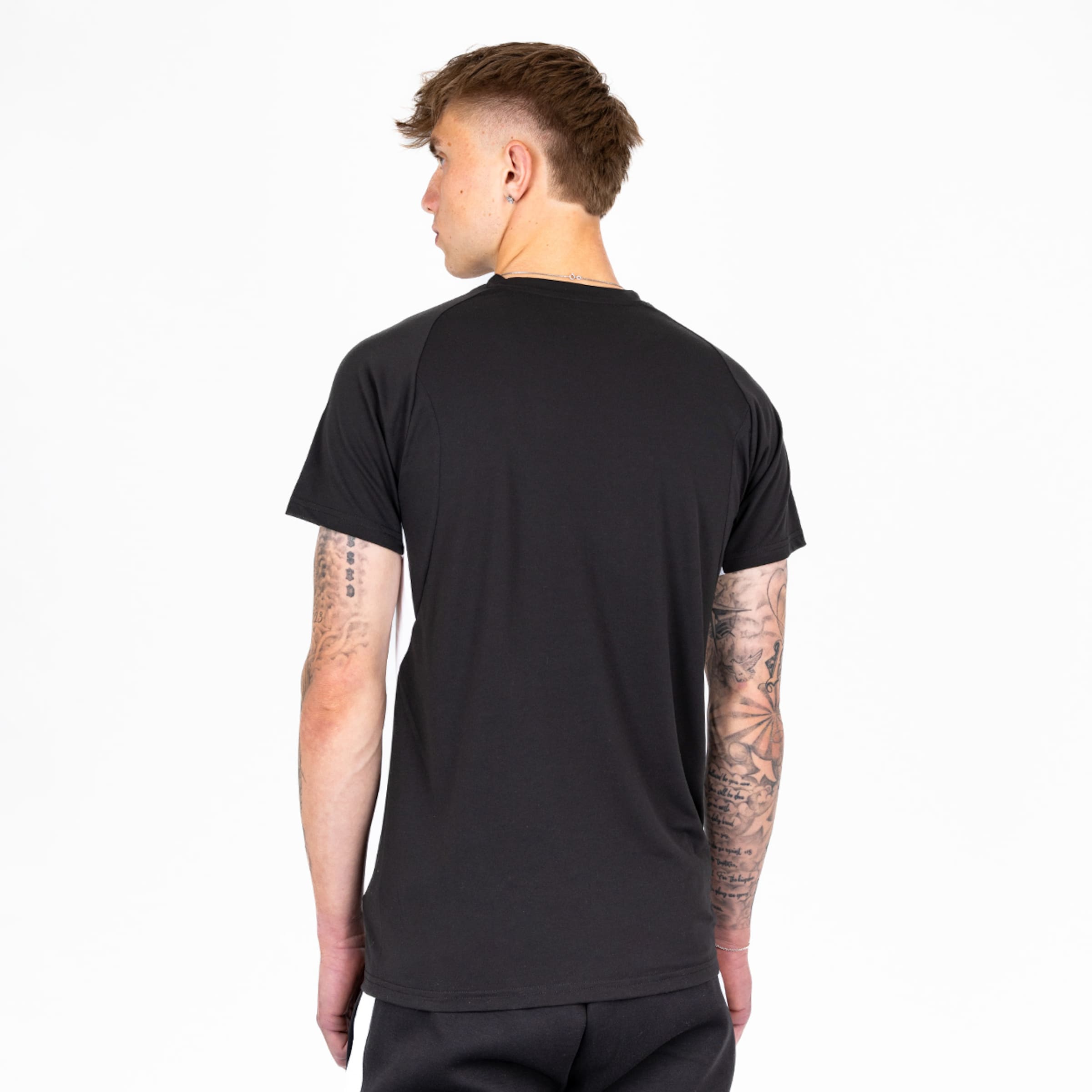 Junger Mann mit Tattoos sieht von hinten in einem schwarzen T-Shirt aus.