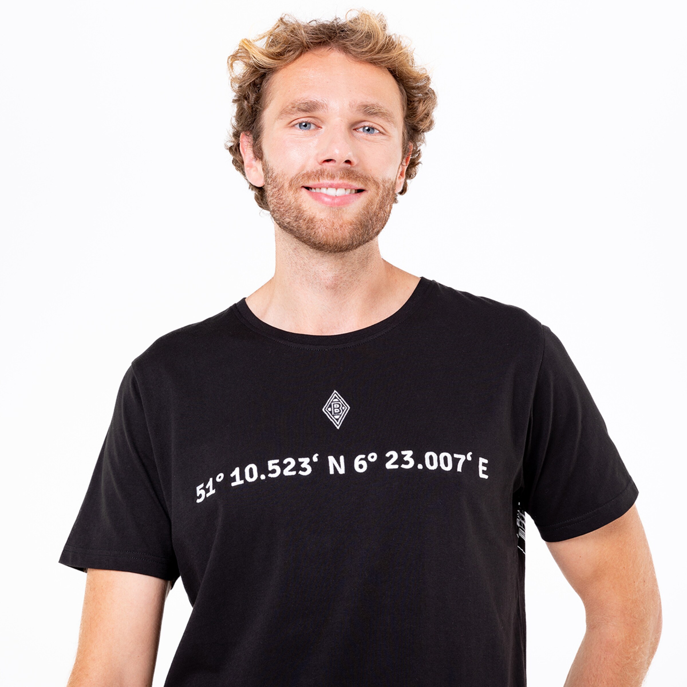 Mann mit lockigem Haar trägt ein schwarzes T-Shirt mit Koordinaten auf der Vorderseite.