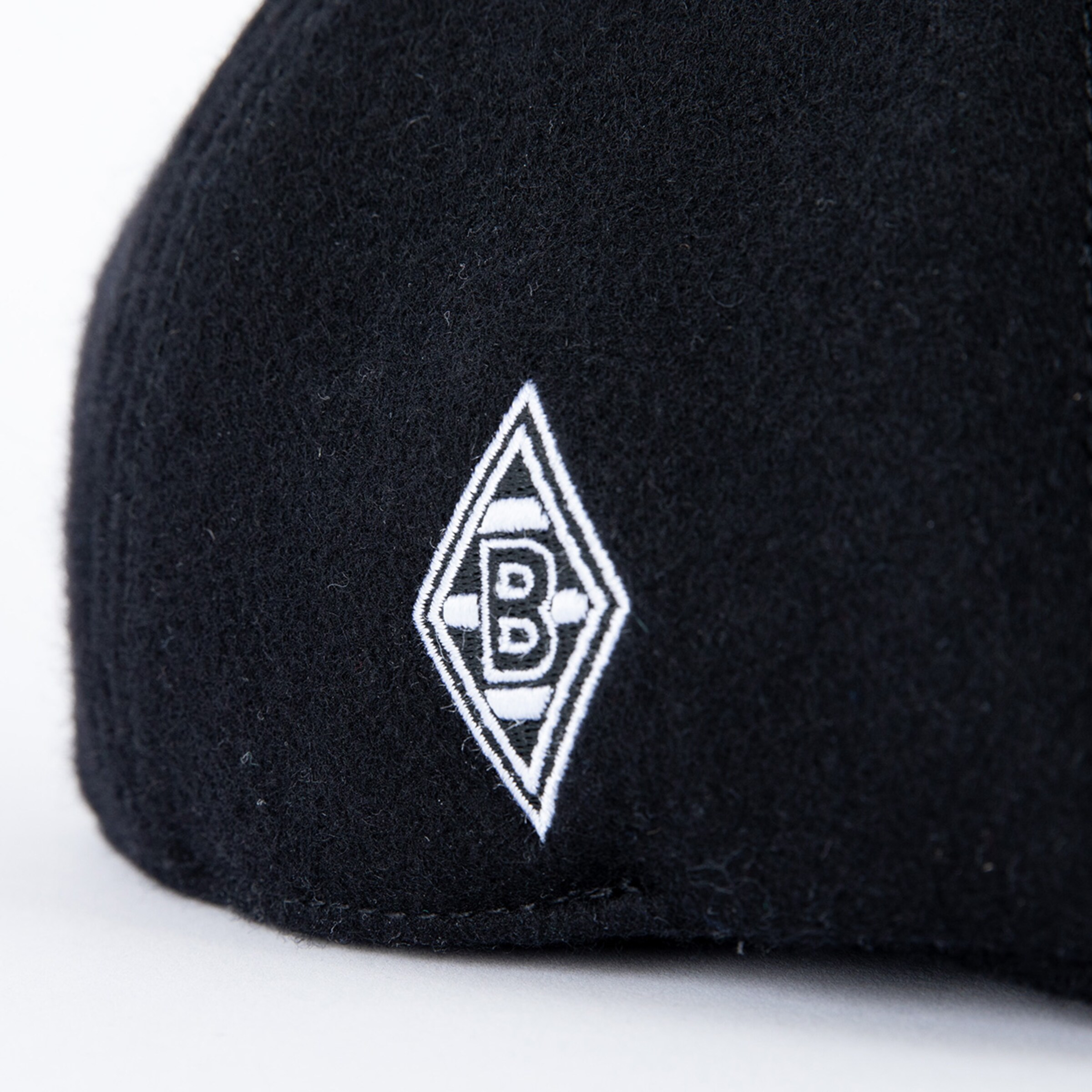 Nahaufnahme einer schwarzen Kappe aus Filz mit dem weiß gestickten Logo von Borussia Mönchengladbach (Raute mit B).