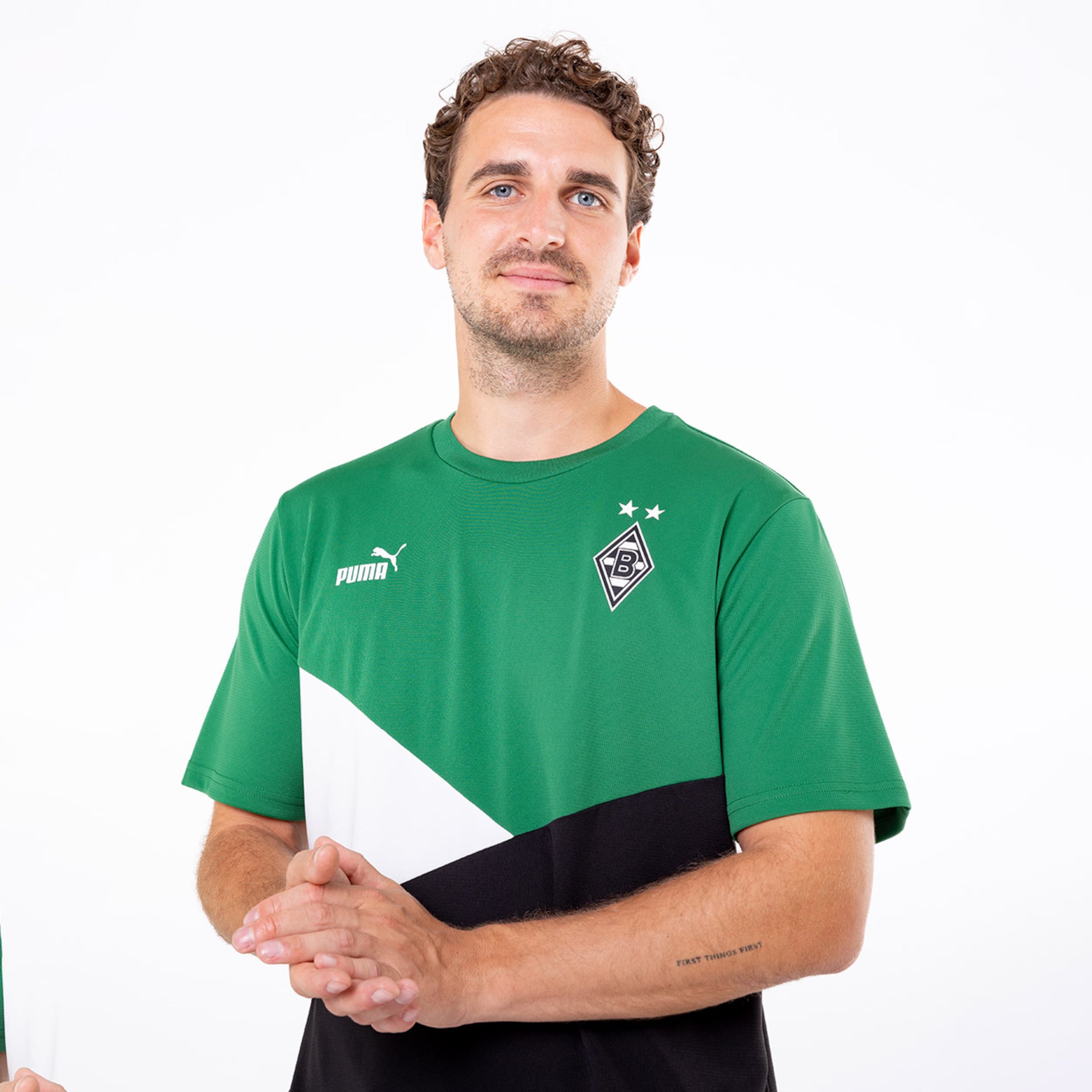 Ein Spieler von Borussia Mönchengladbach in einem grünen Trikot mit schwarzem und weißem Design lächelnd.