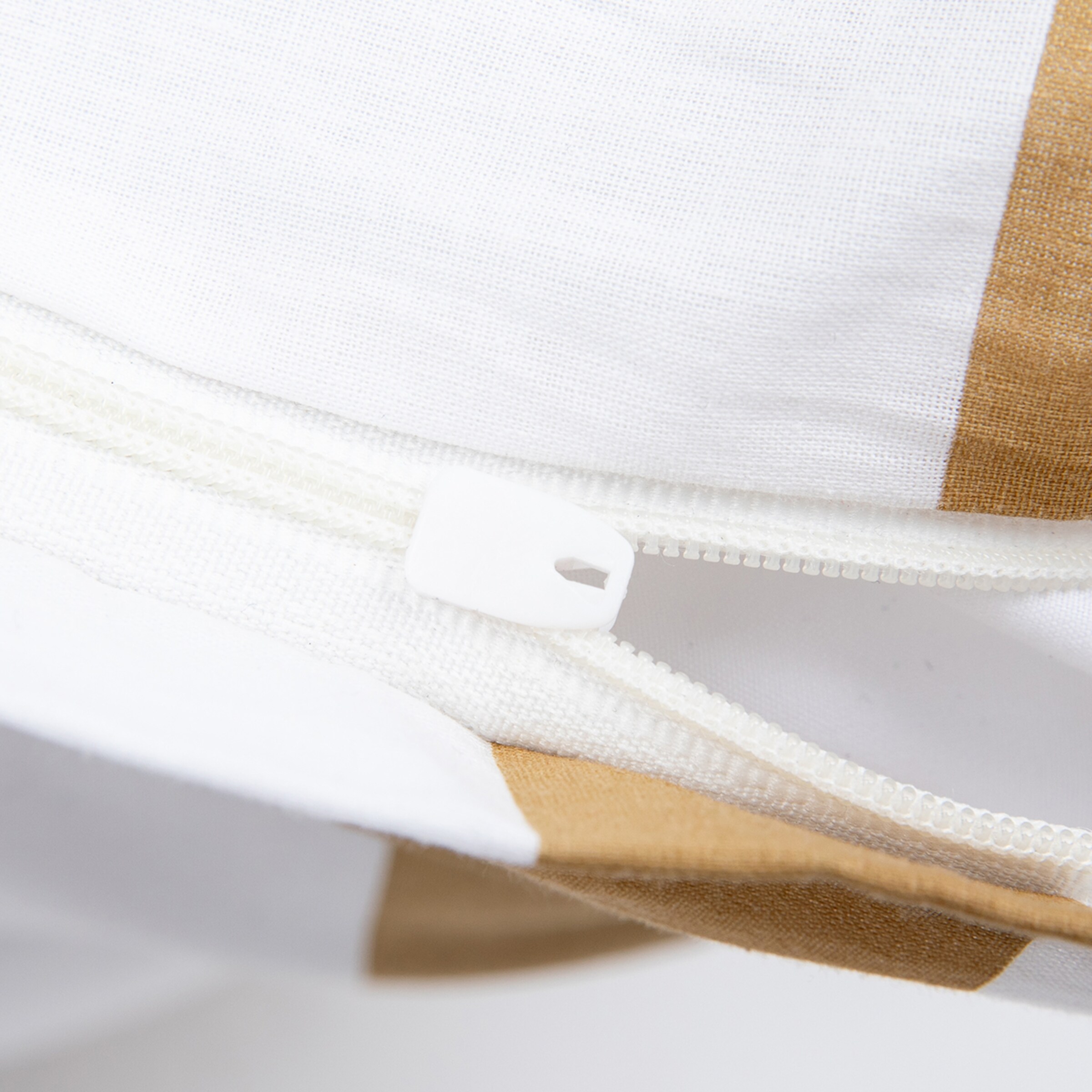 Nahaufnahme eines weißen Reißverschlusses an einem weiß und braun gestreiften Kissenbezug.