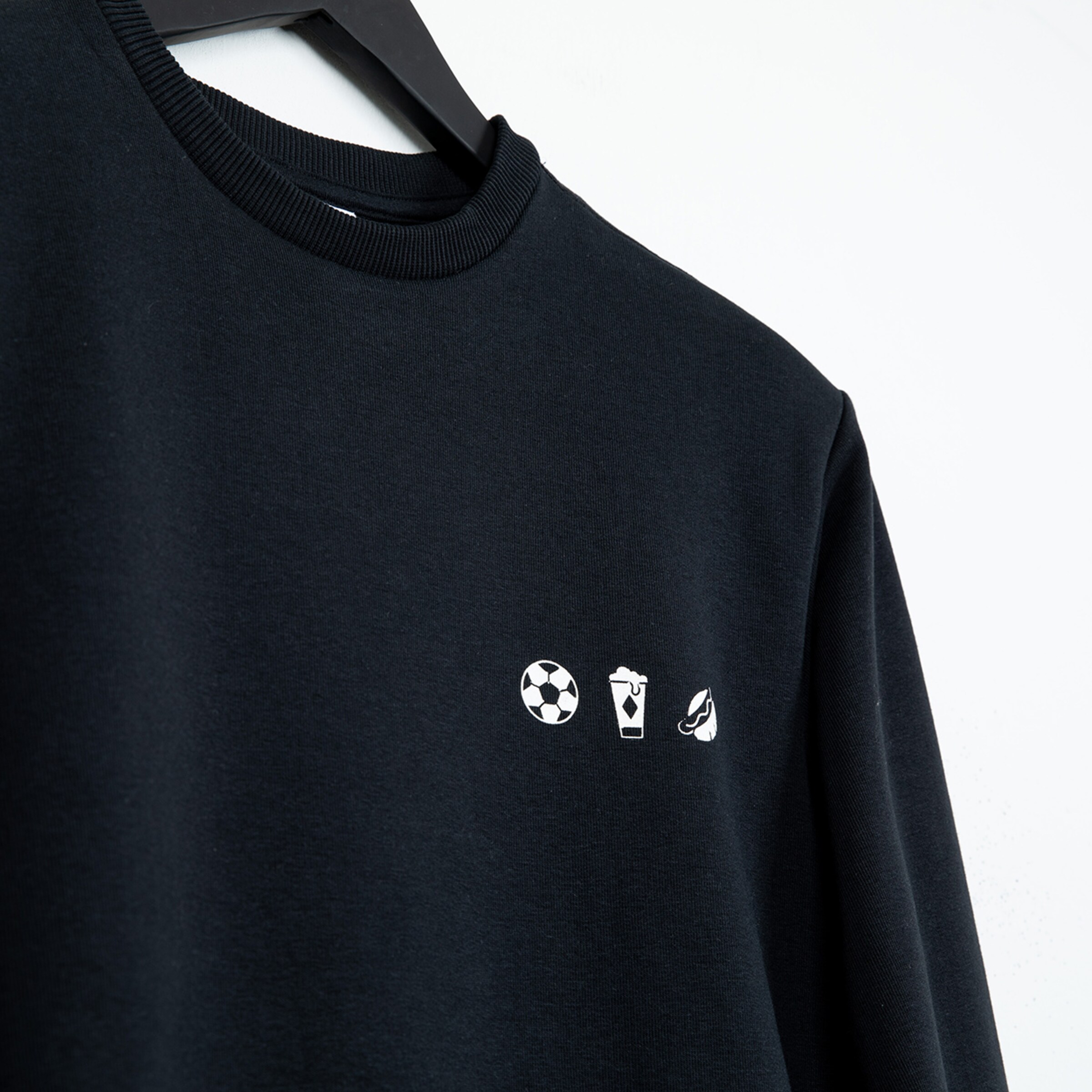Schwarzer Pullover mit drei weißen Symbolen: Fußball Trinkbecher Schiedsrichterpfeife.