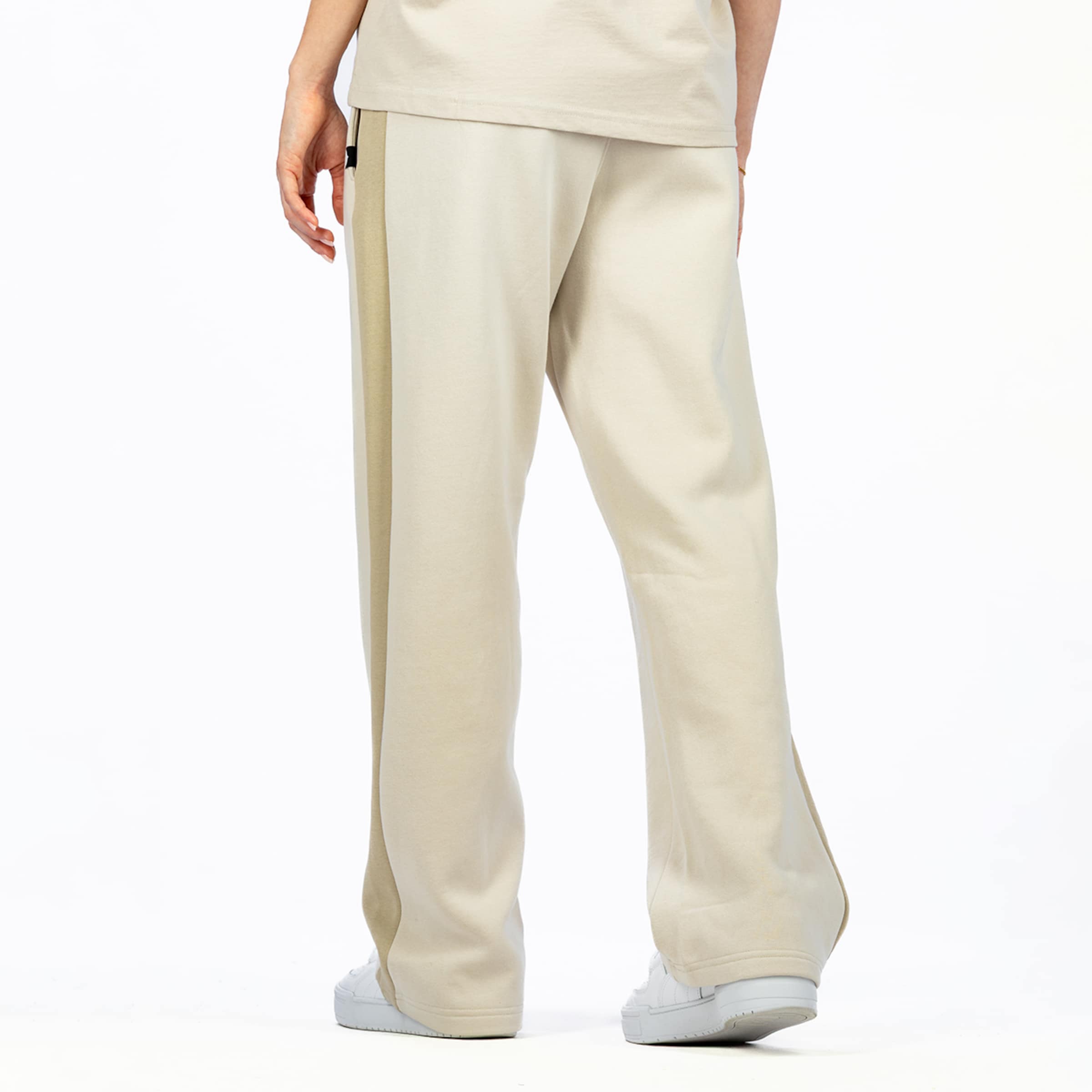 A person seen from behind, wearing a light beige t-shirt and matching wide-leg trousers with a darker beige stripe down the side. The person is also wearing white sneakers.
