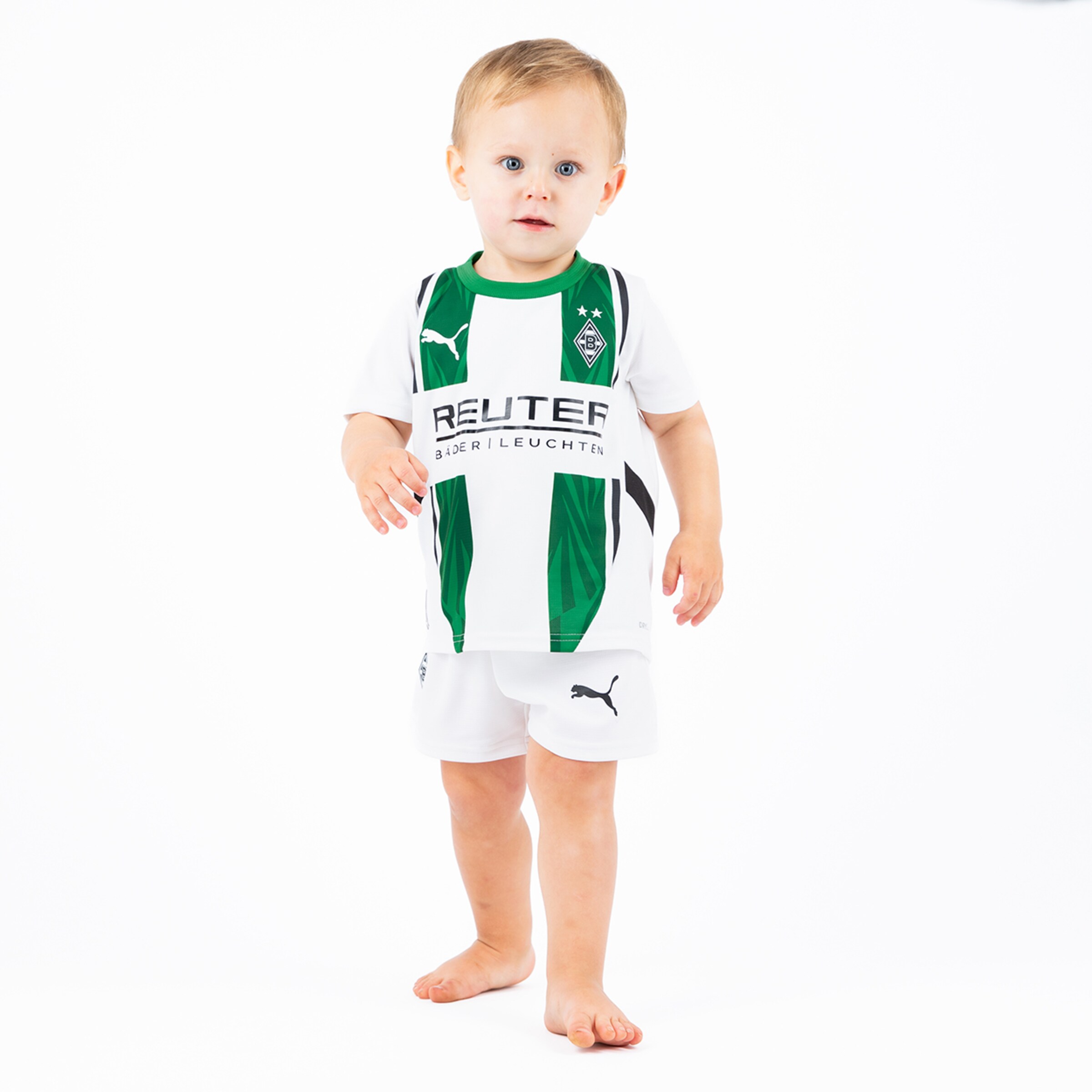 Ein kleines Kind in einem Borussia Mönchengladbach Trikot mit Shorts steht barfuß.