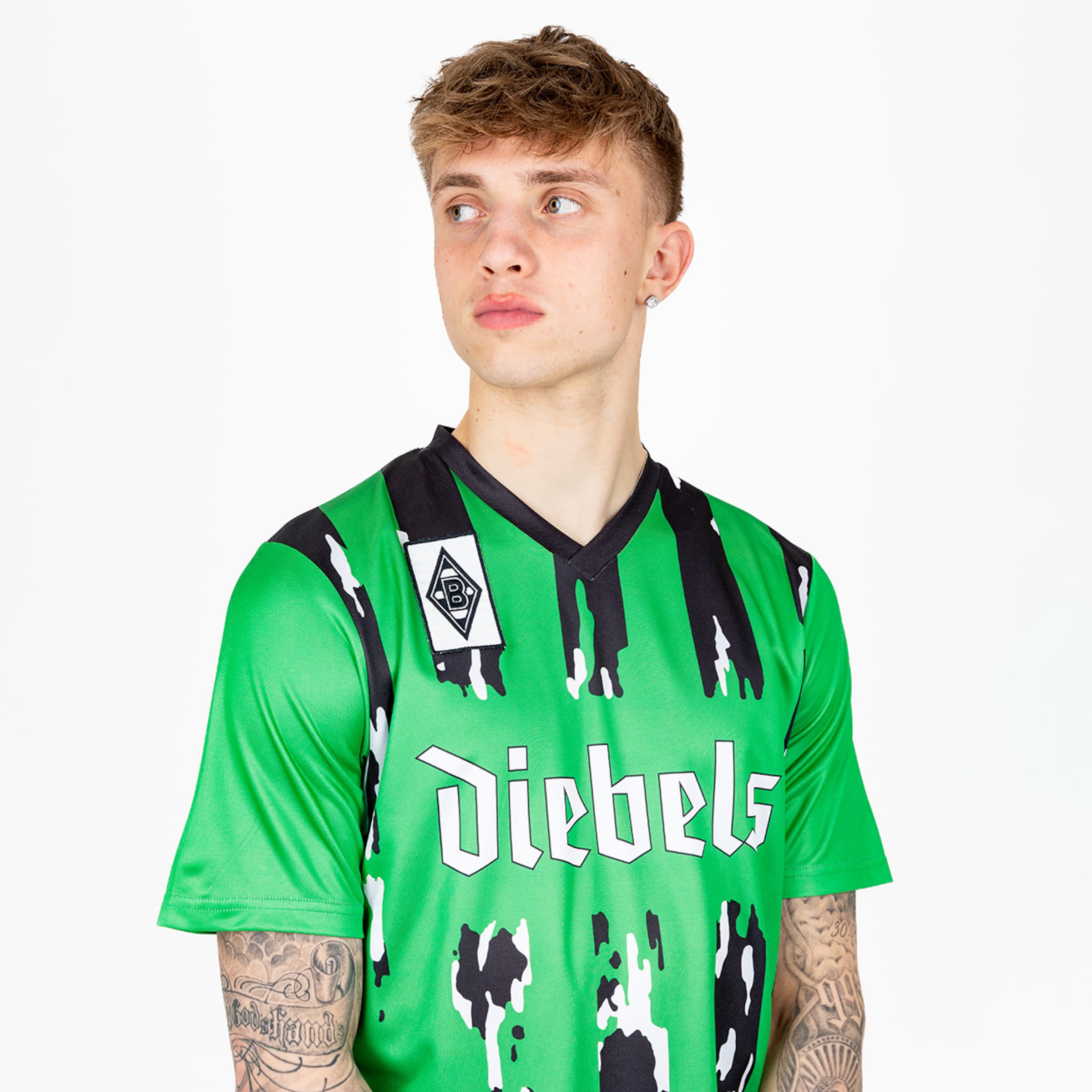 Junger Mann in einem leuchtend grünen Fußballtrikot mit bunten Mustern und dem Schriftzug Diebels.