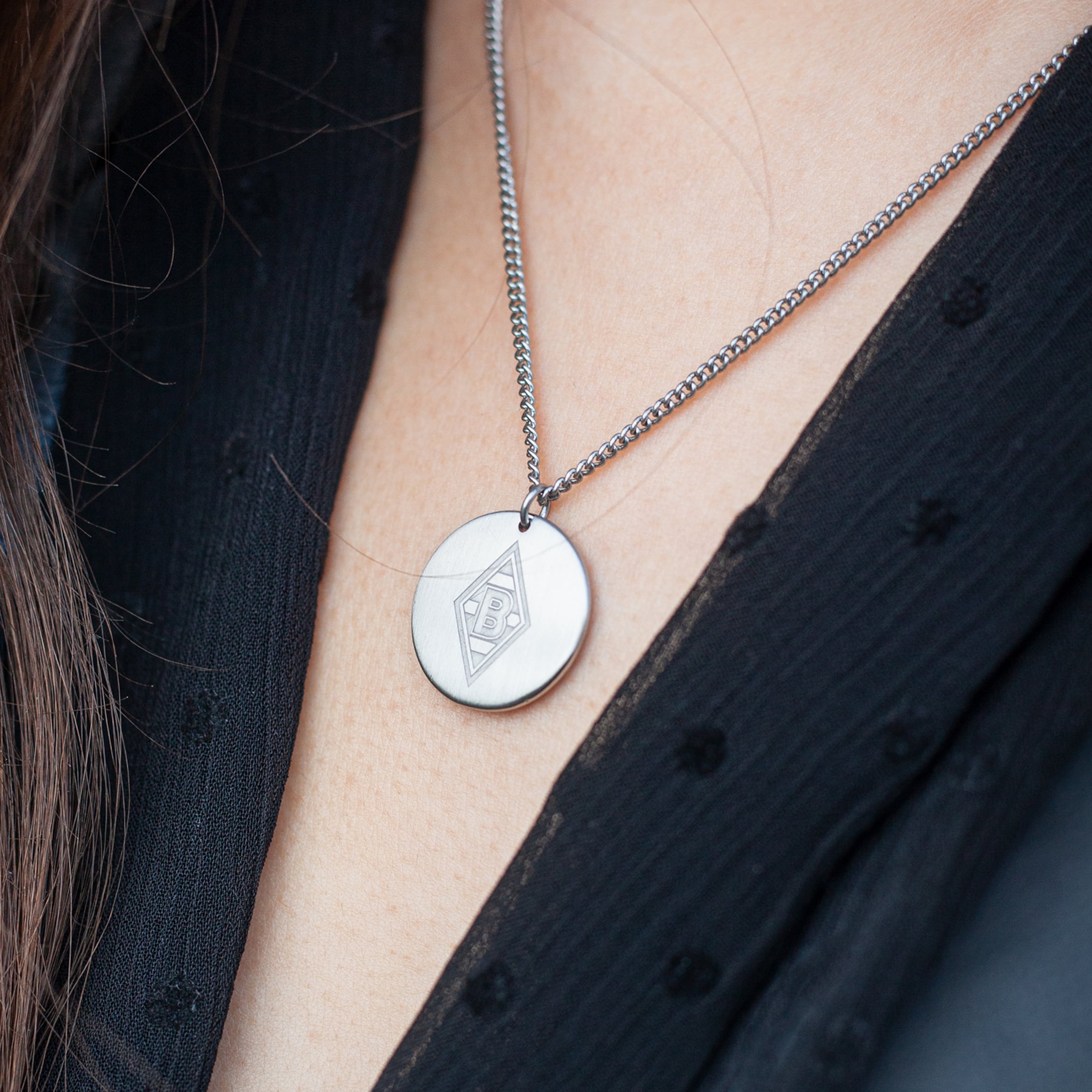 Eine Halskette mit einem runden Anhänger der das Logo von Borussia Mönchengladbach zeigt.