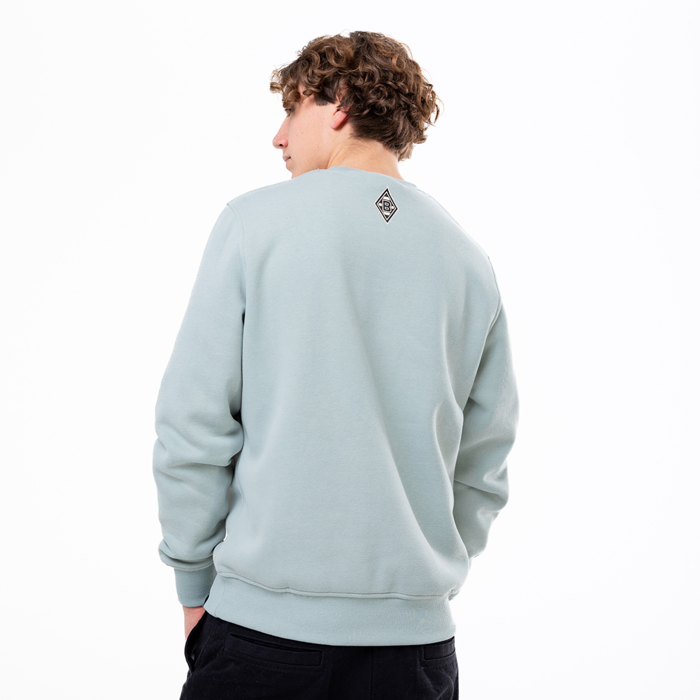 Jugendlicher mit lockigen Haaren trägt einen hellblauen Sweatshirt Ansicht von hinten mit einem Logo auf dem Rücken.