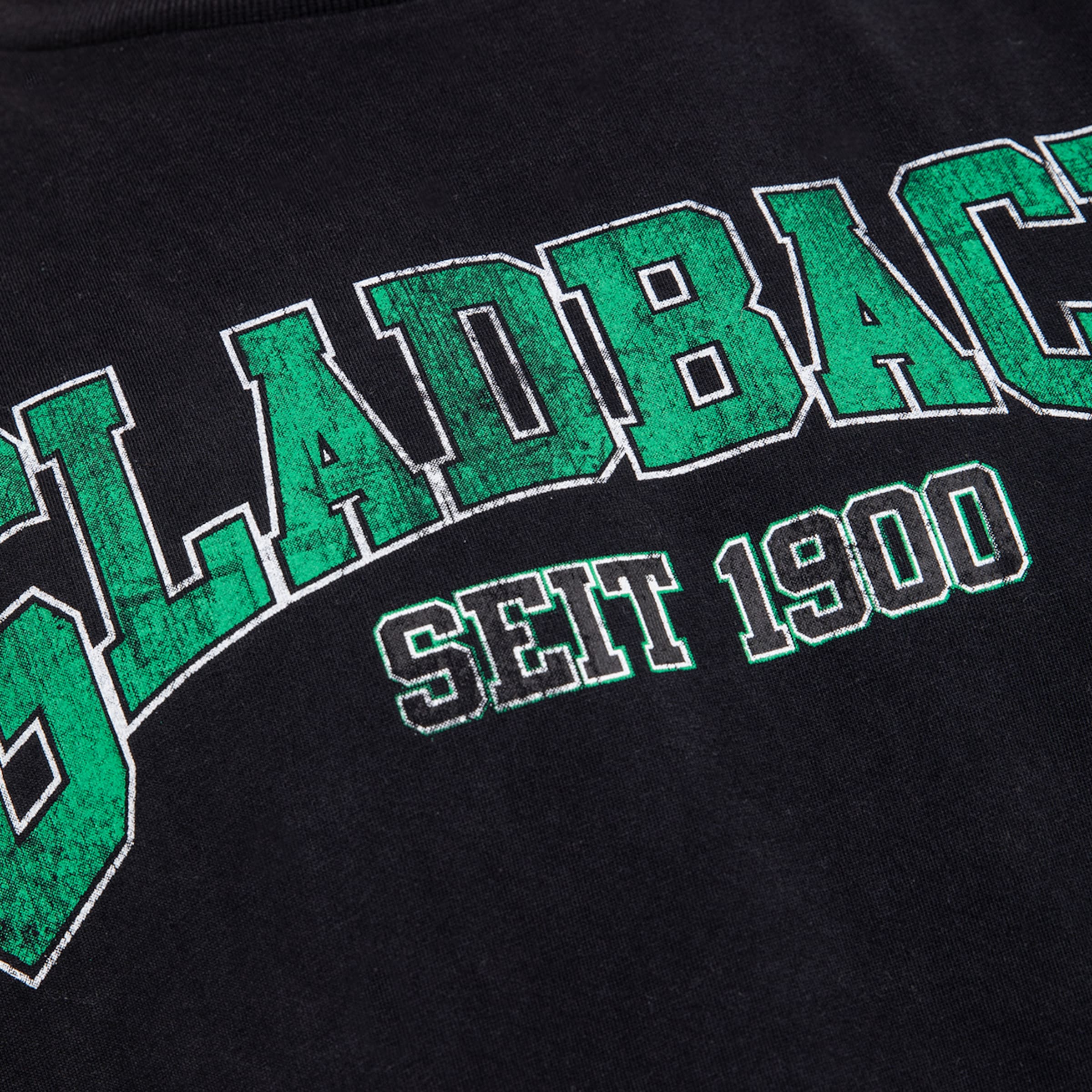 Grüner Vintage-Schriftzug „GLADBACH SEIT 1900“ mit weißer Kontur auf schwarzem Stoff.