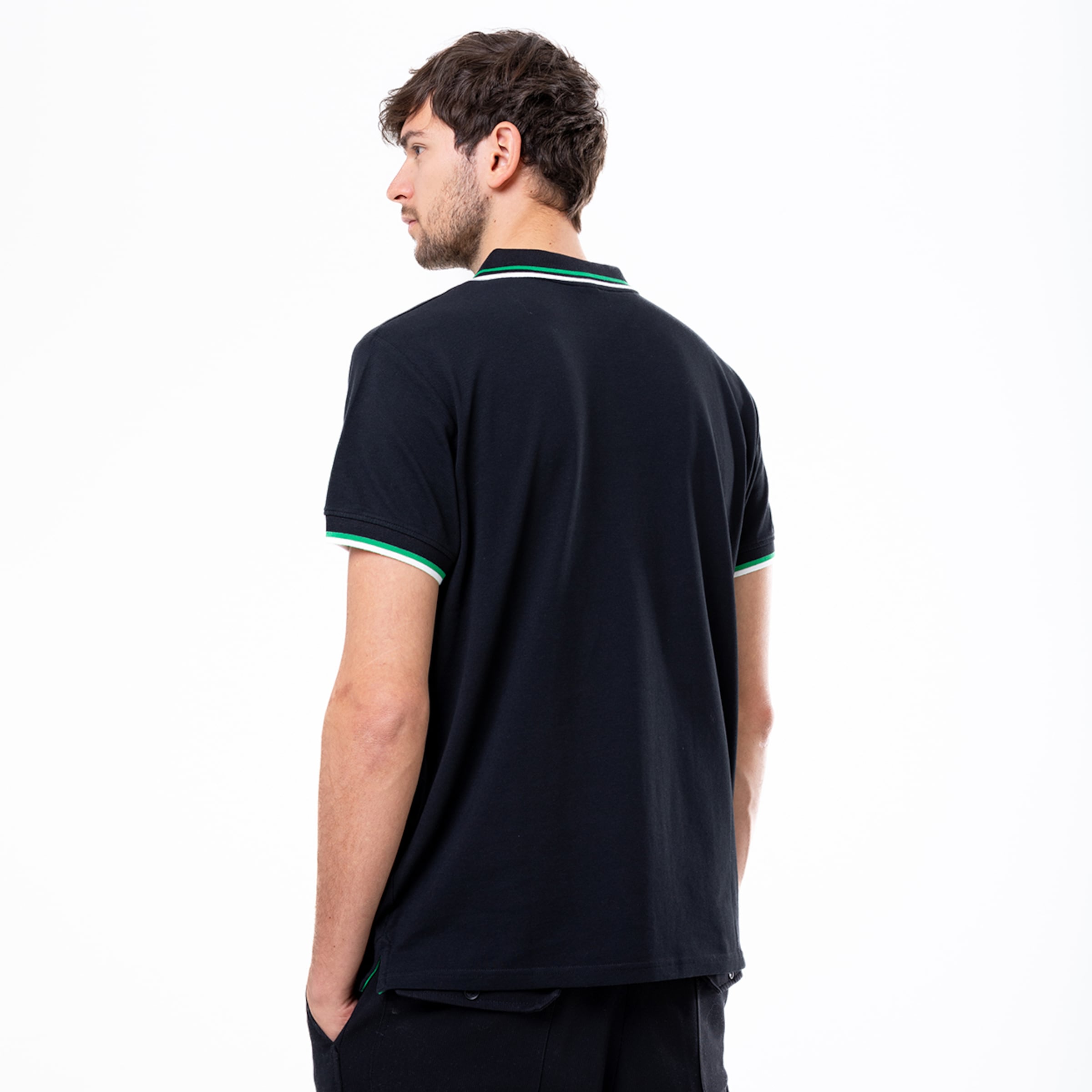 Back view of a man wearing a black polo shirt with green and white tipped collar and sleeve cuffs against a white background.