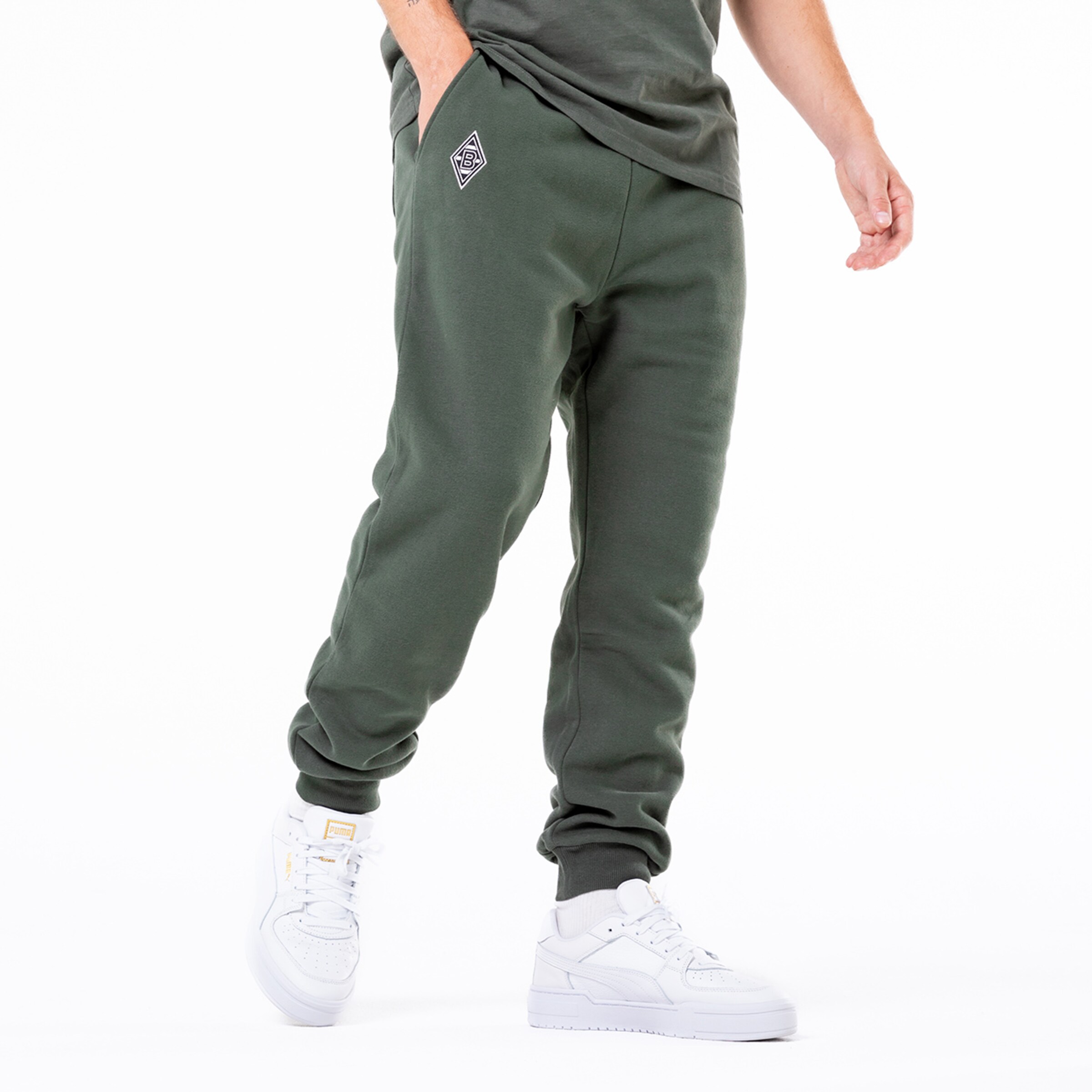 Grüne Jogginghose mit seitlichen Taschen und gesticktem Logo kombiniert mit weißen Sneakers.