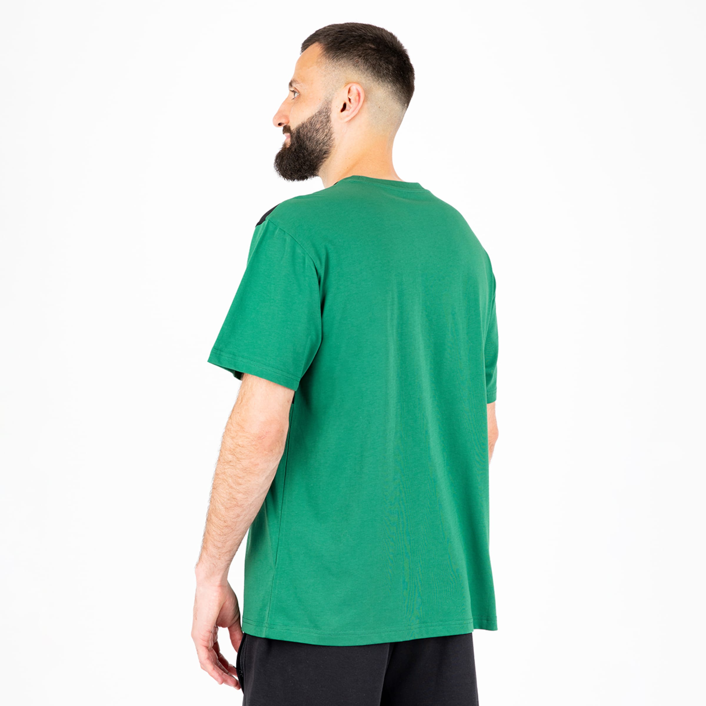 Rückenansicht eines bärtigen Mannes in grünem T-Shirt und schwarzen Shorts vor weißem Hintergrund.