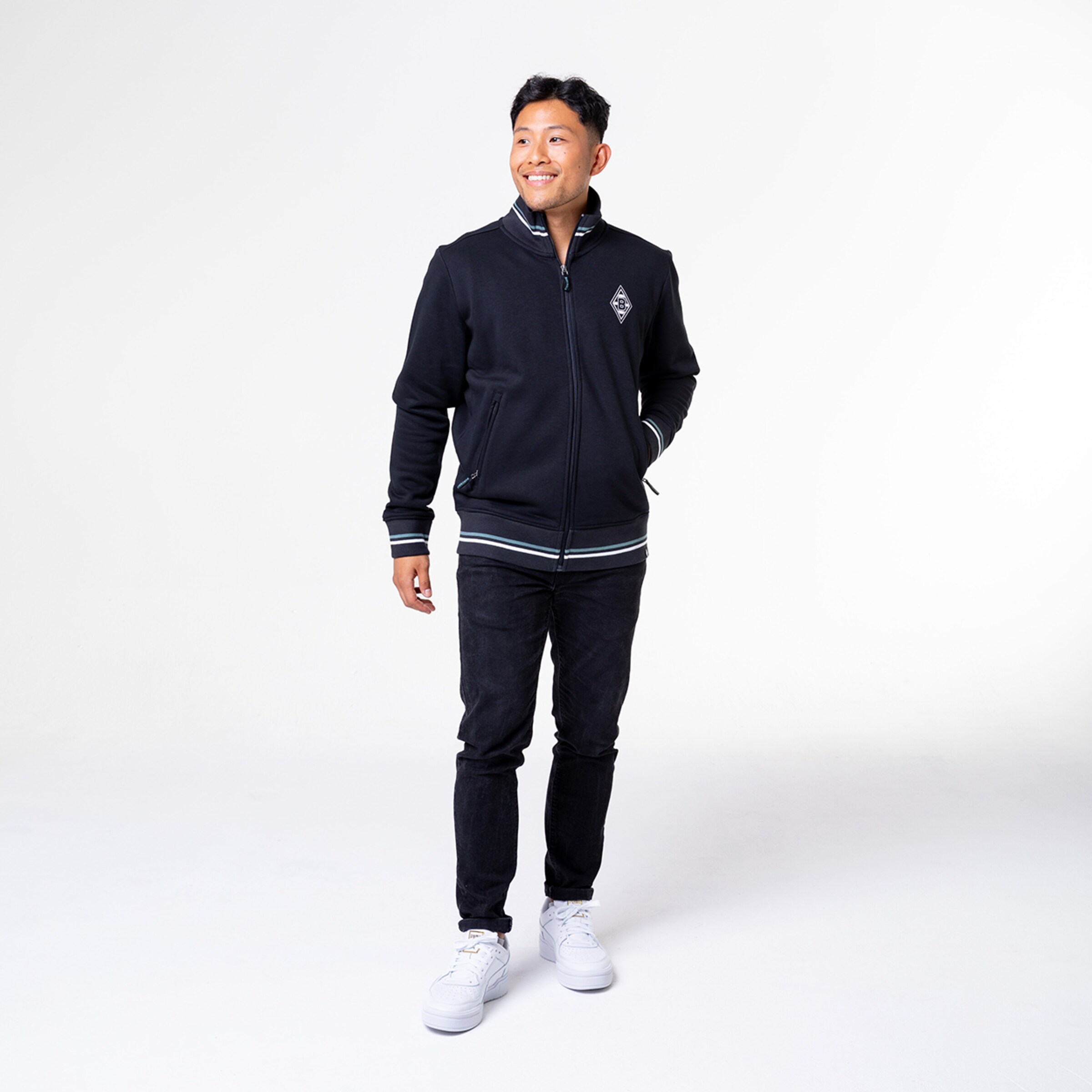 Mann steht in schwarzer Jacke und weißen Sneakern.