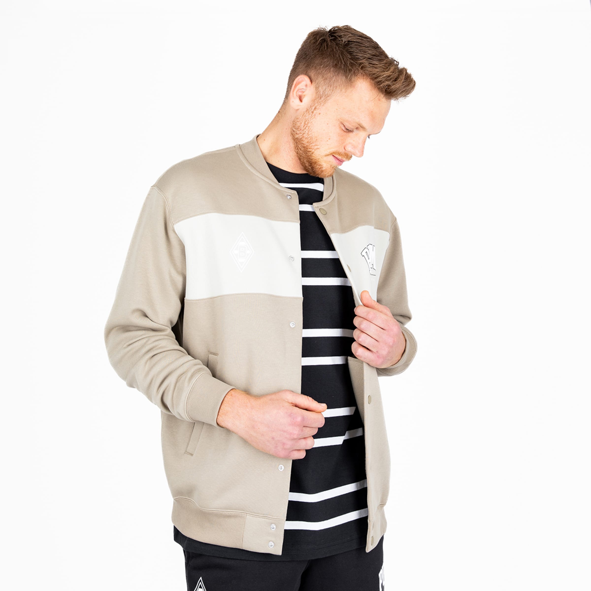 Mann in beiger Jacke mit weißem Streifen und gestreiftem T-Shirt.