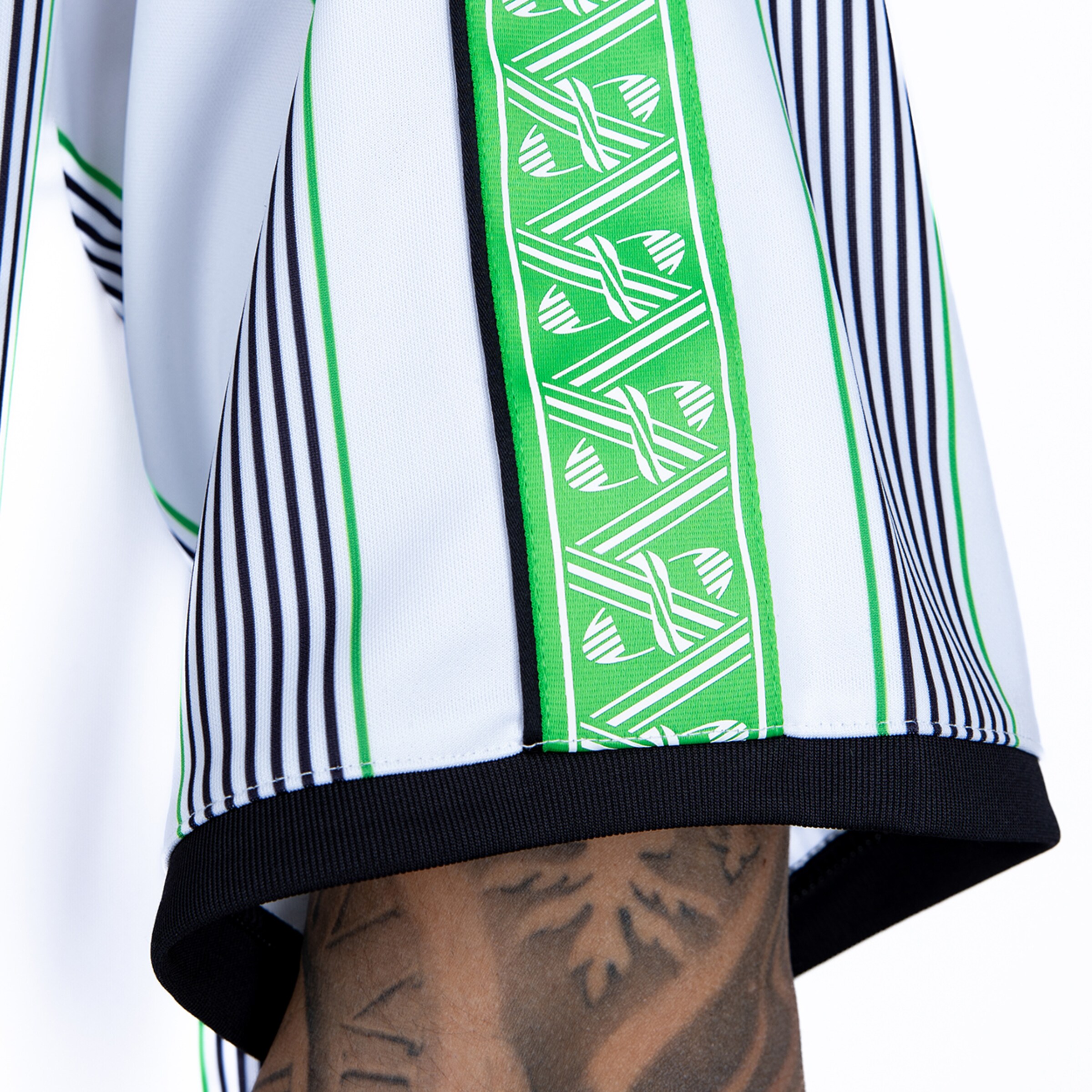 Close-up of a white jersey sleeve with black stripes, a green logo tape, and a black ribbed cuff.