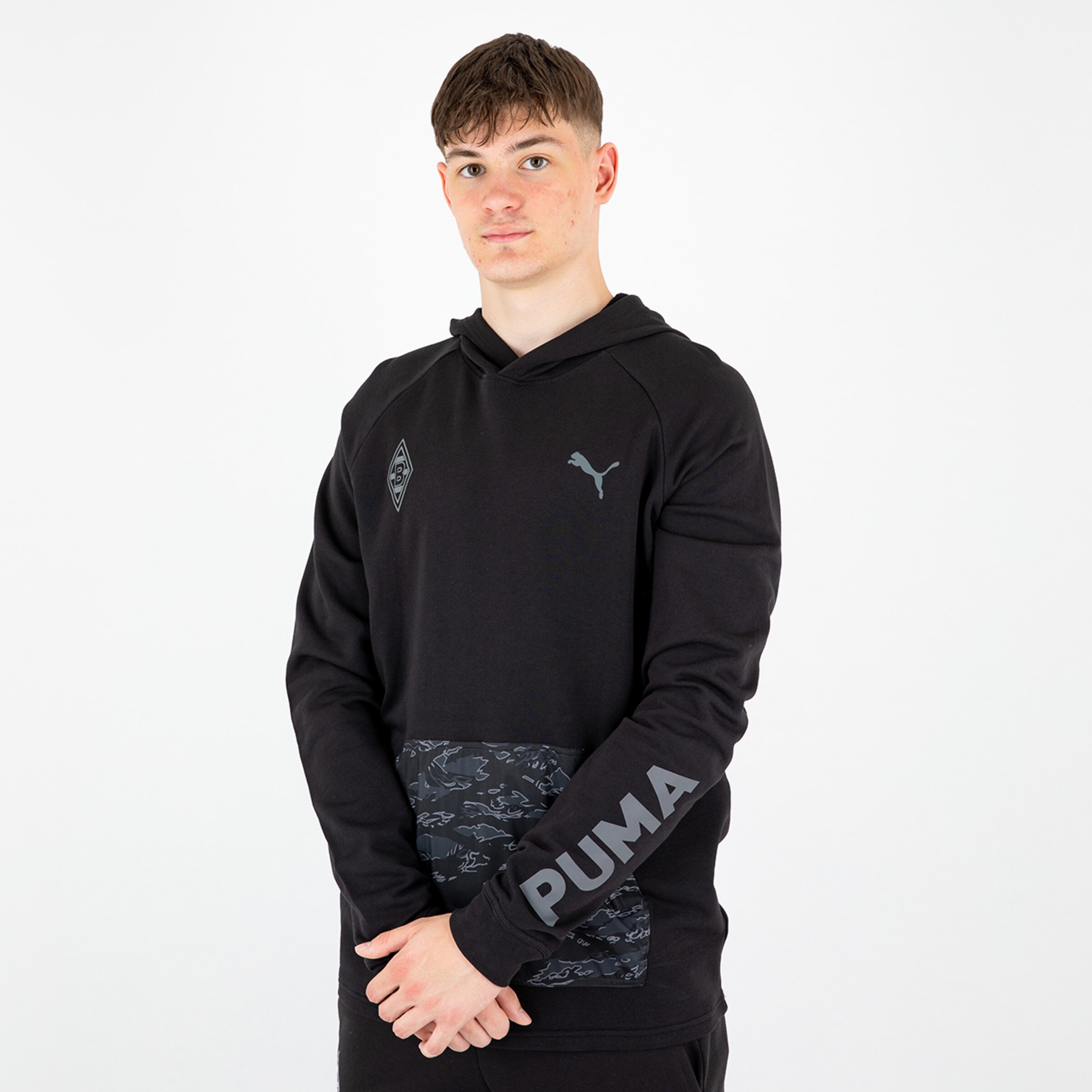 Junger Mann in schwarzem Hoodie mit Puma-Logo und Borussia Mönchengladbach-Emblem steht mit verschränkten Armen.