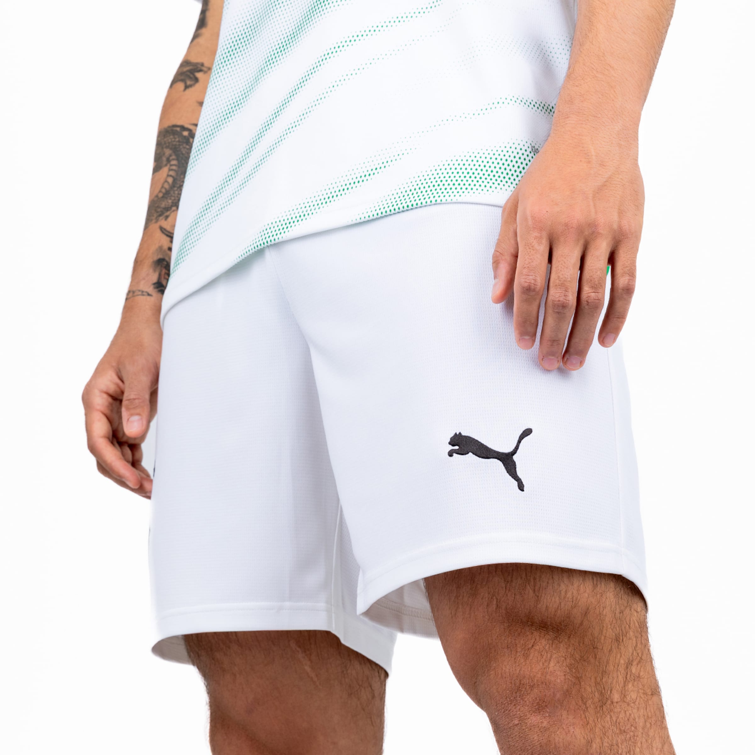 Nahaufnahme einer weißen Puma Sport-Shorts mit schwarzem Logo und einem weiß-grün gemusterten Trikot.