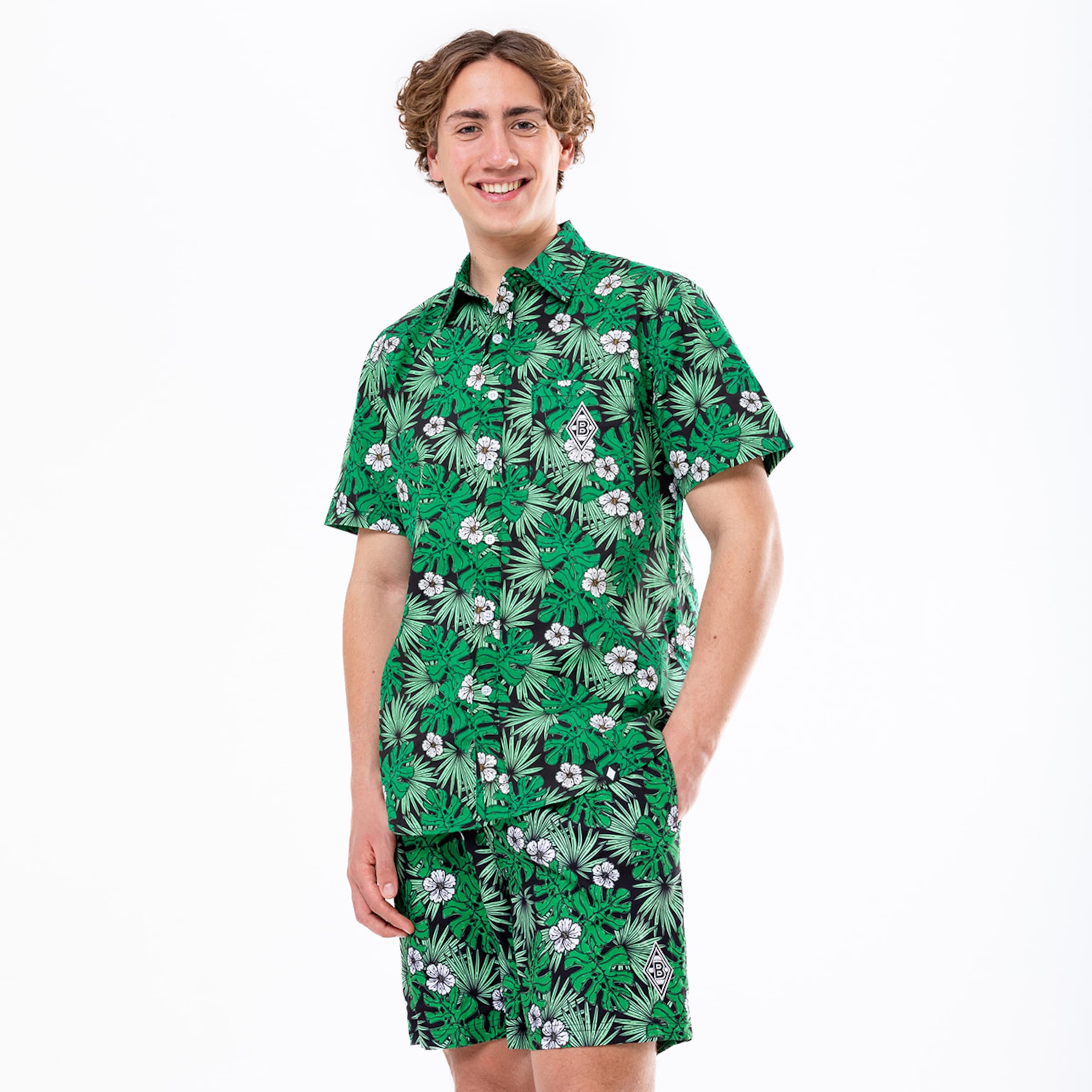 Mann in einem tropischen Muster-T-Shirt und Shorts mit grünem Hintergrund.
