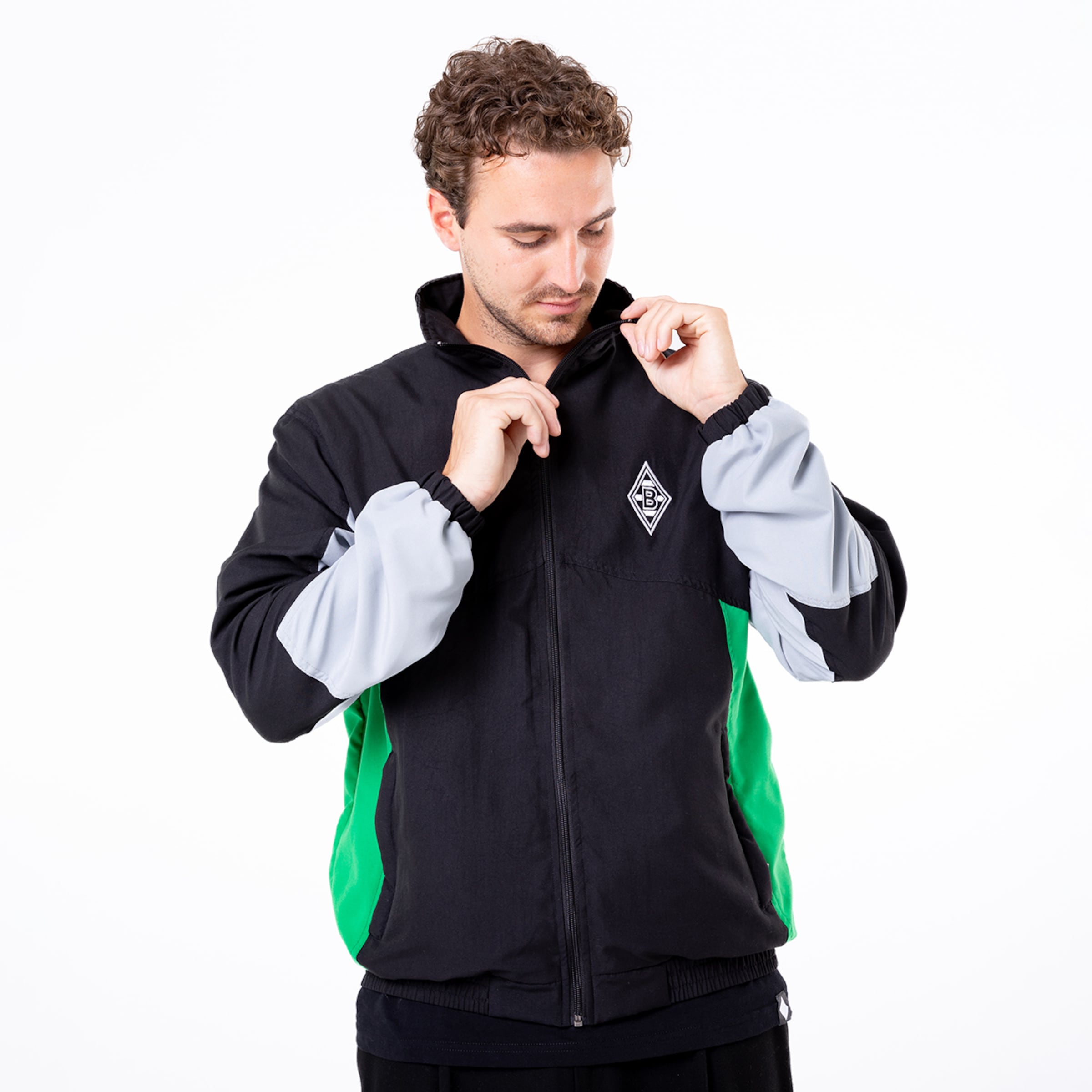 Mann trägt eine schwarze Jacke mit grauen und grünen Details er schließt den Reißverschluss.