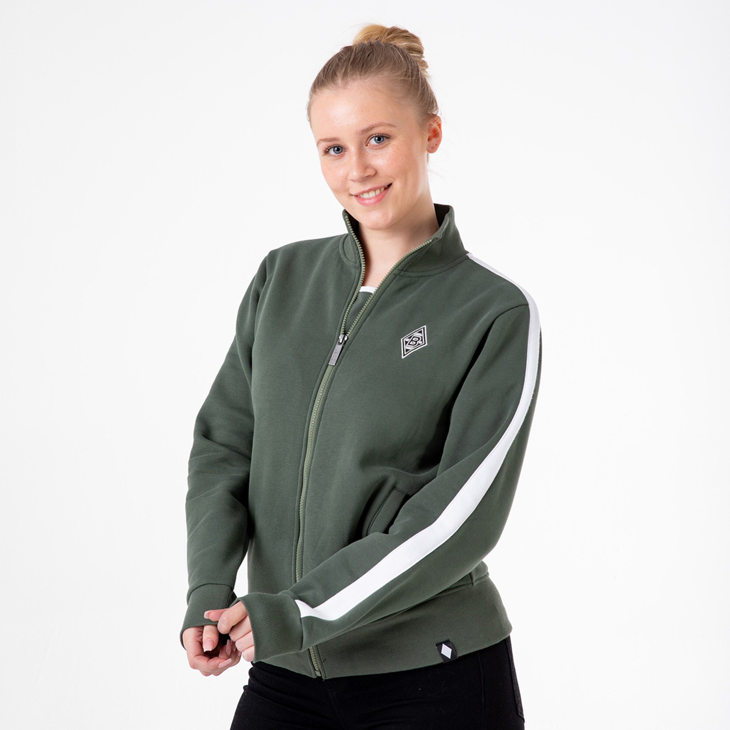 Dame in olivafarbenem Fleecejacke mit weißem Streifen lächelt und hält die Hände zusammen.