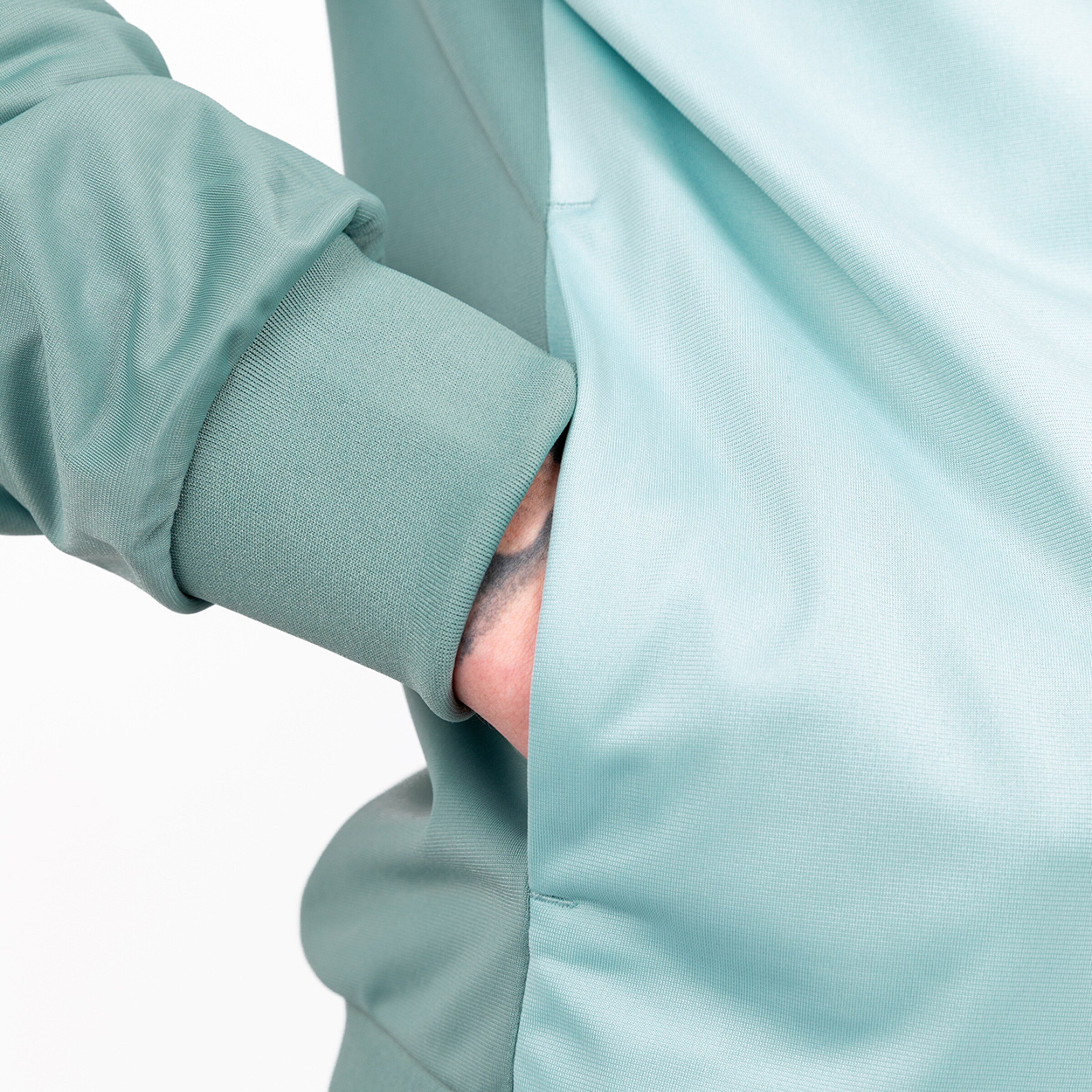 Close-up of a green sweatshirt showing a sleeve and a hand reaching into a side pocket.