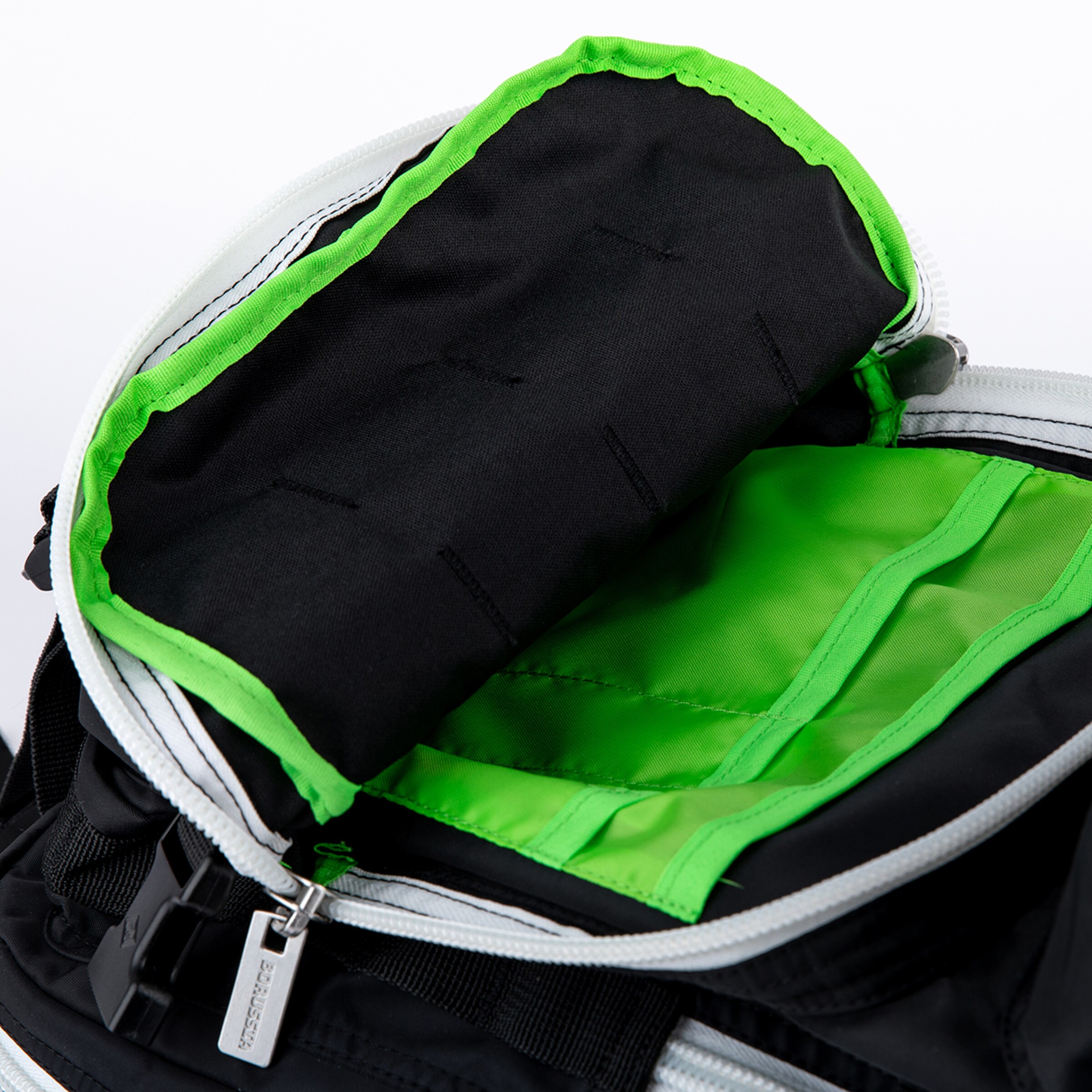 Top-down view of an open black bag or backpack, featuring a bright green interior lining with separate compartments. The zipper is white, and a metal tag on the zipper pull is visible with the word “BORUSSIA” on it.