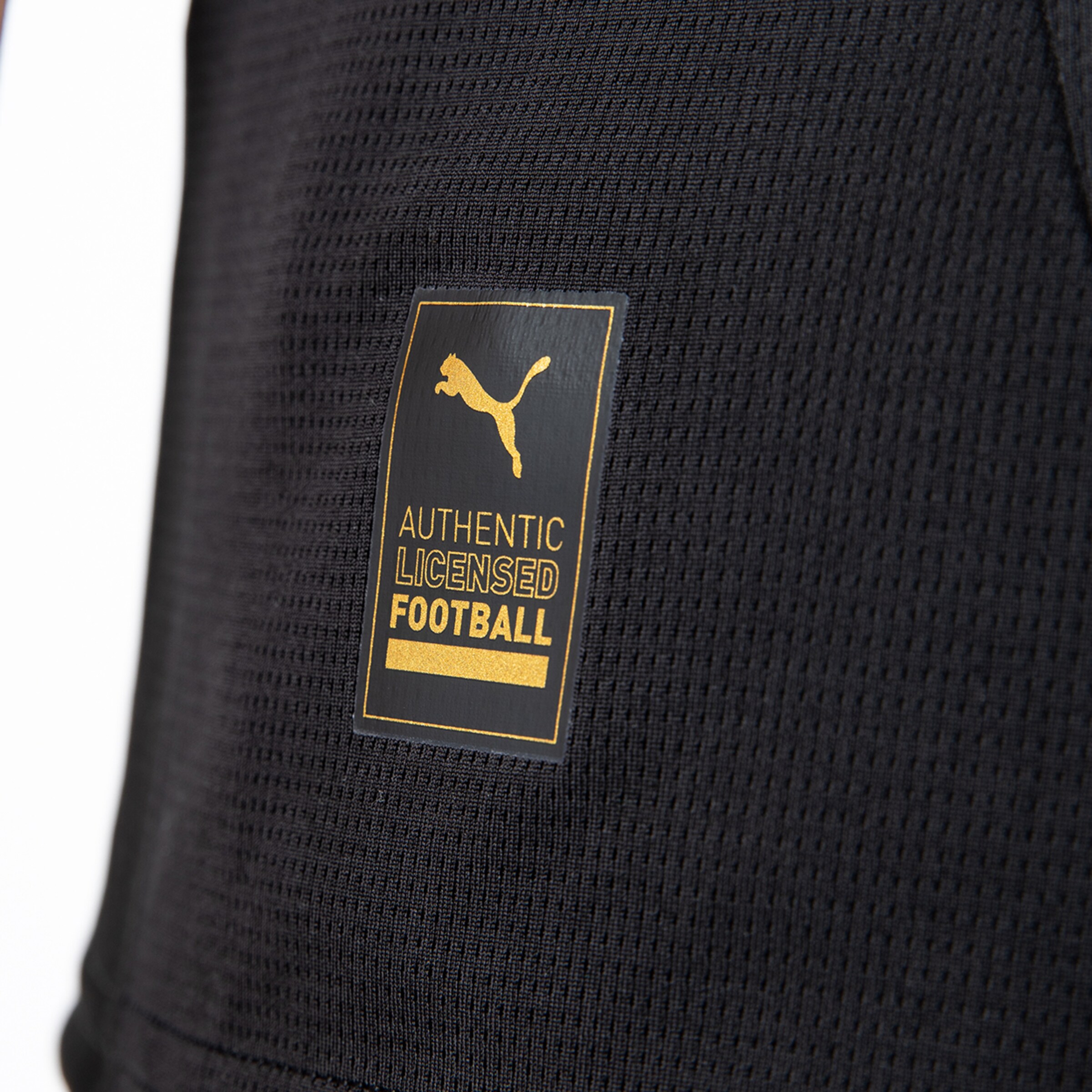Details des Puma-Labels für lizenzierten Fußball in goldener Schrift auf schwarzem Stoff.