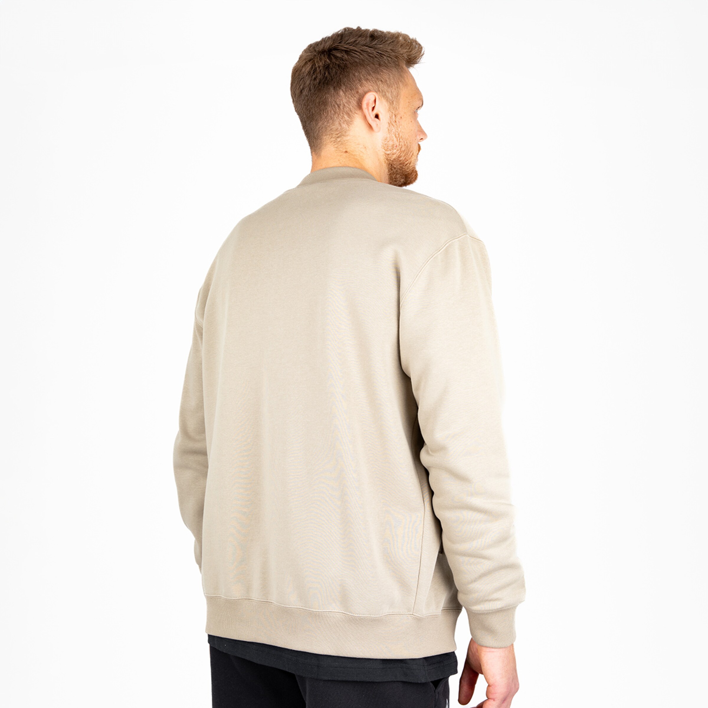 Mann in einem hellbeigen Sweatshirt steht mit dem Rücken zur Kamera.