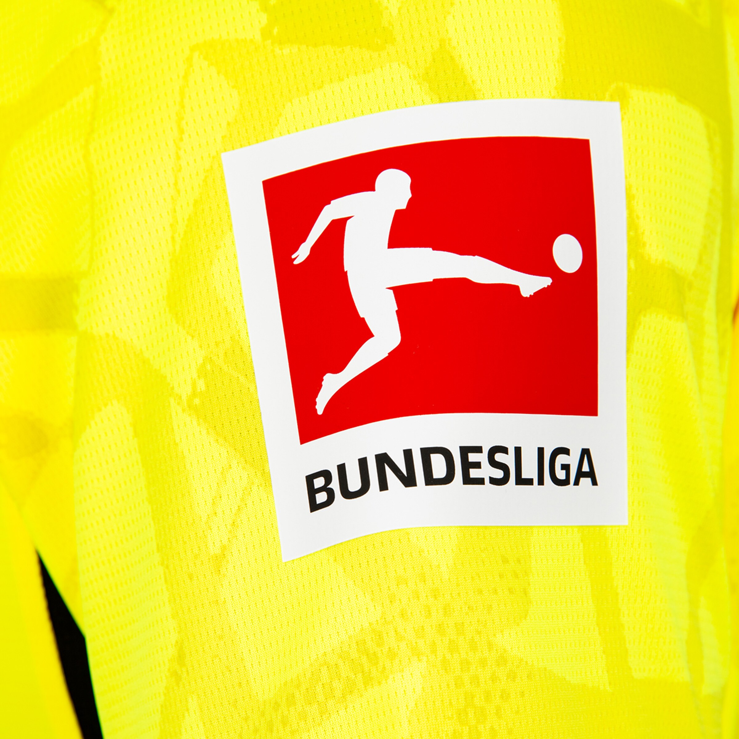 Bundesliga-Logo mit Fußballer-Silhouette auf rotem Hintergrund und schwarzem Text, auf gelbem Trikotstoff.