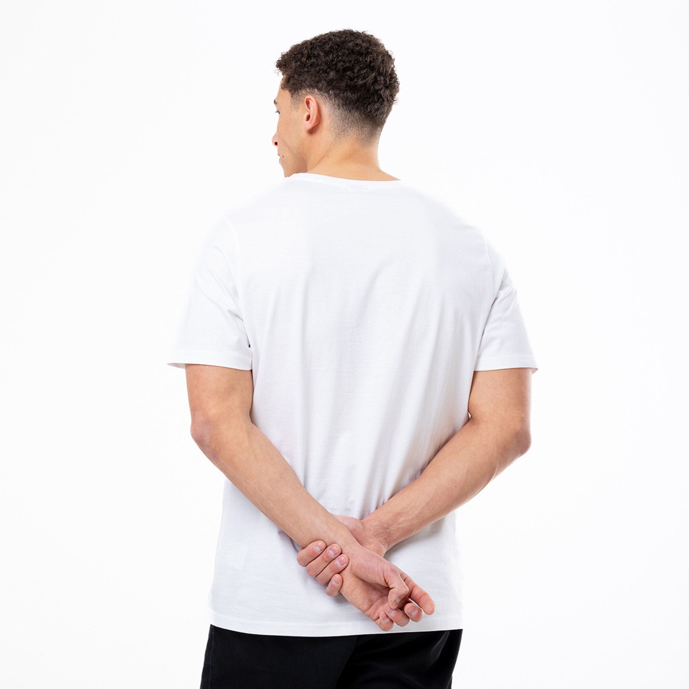 Mann in weißem T-Shirt mit verschränkten Händen hinter dem Rücken.