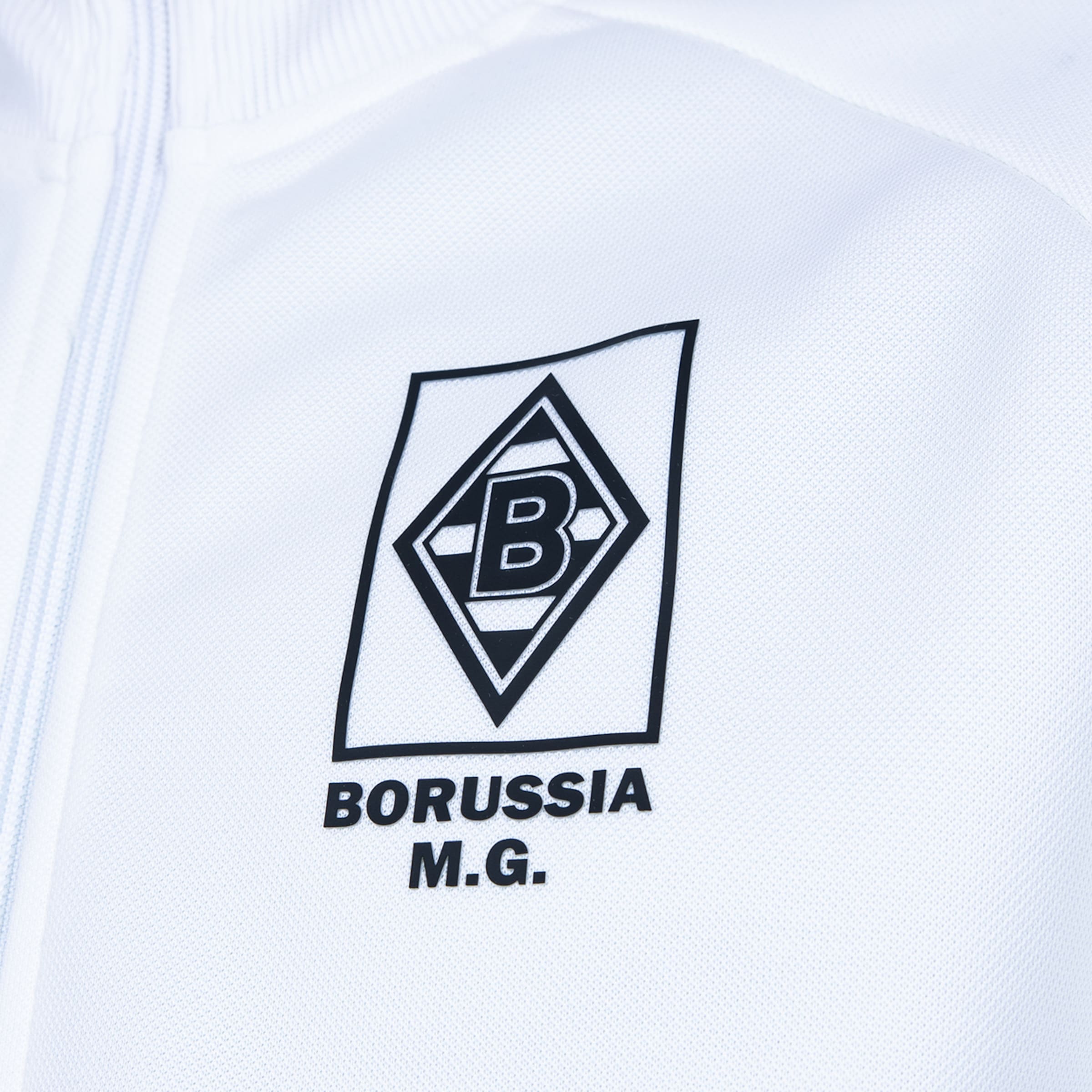 Logo von Borussia Mönchengladbach auf weißer Jacke. Schwarze Raute mit „B“ und dem Schriftzug „BORUSSIA M.G.“ darunter.