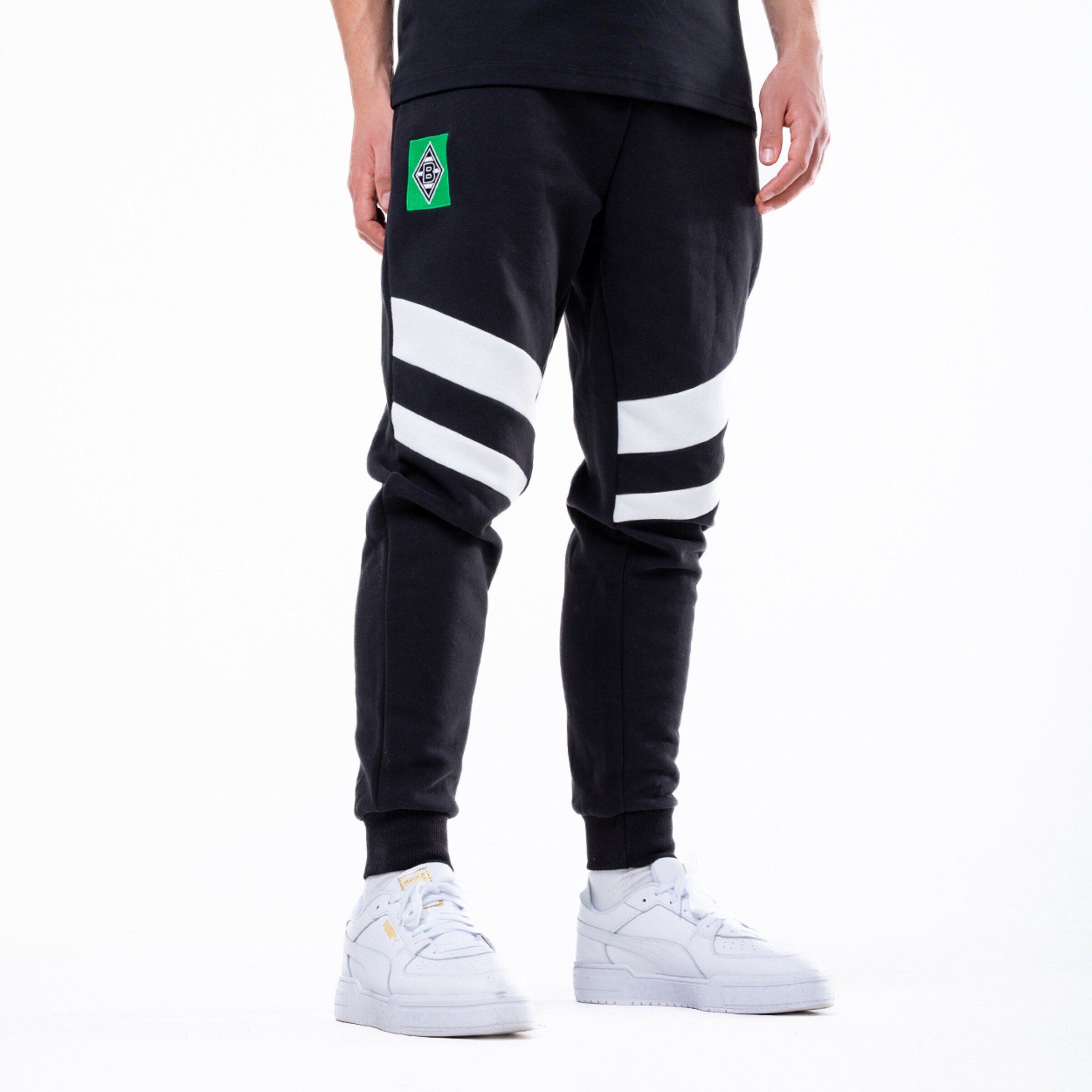 Schwarze Jogginghose mit weißen Querstreifen, Borussia Mönchengladbach Logo und weißen Puma Sneakern.