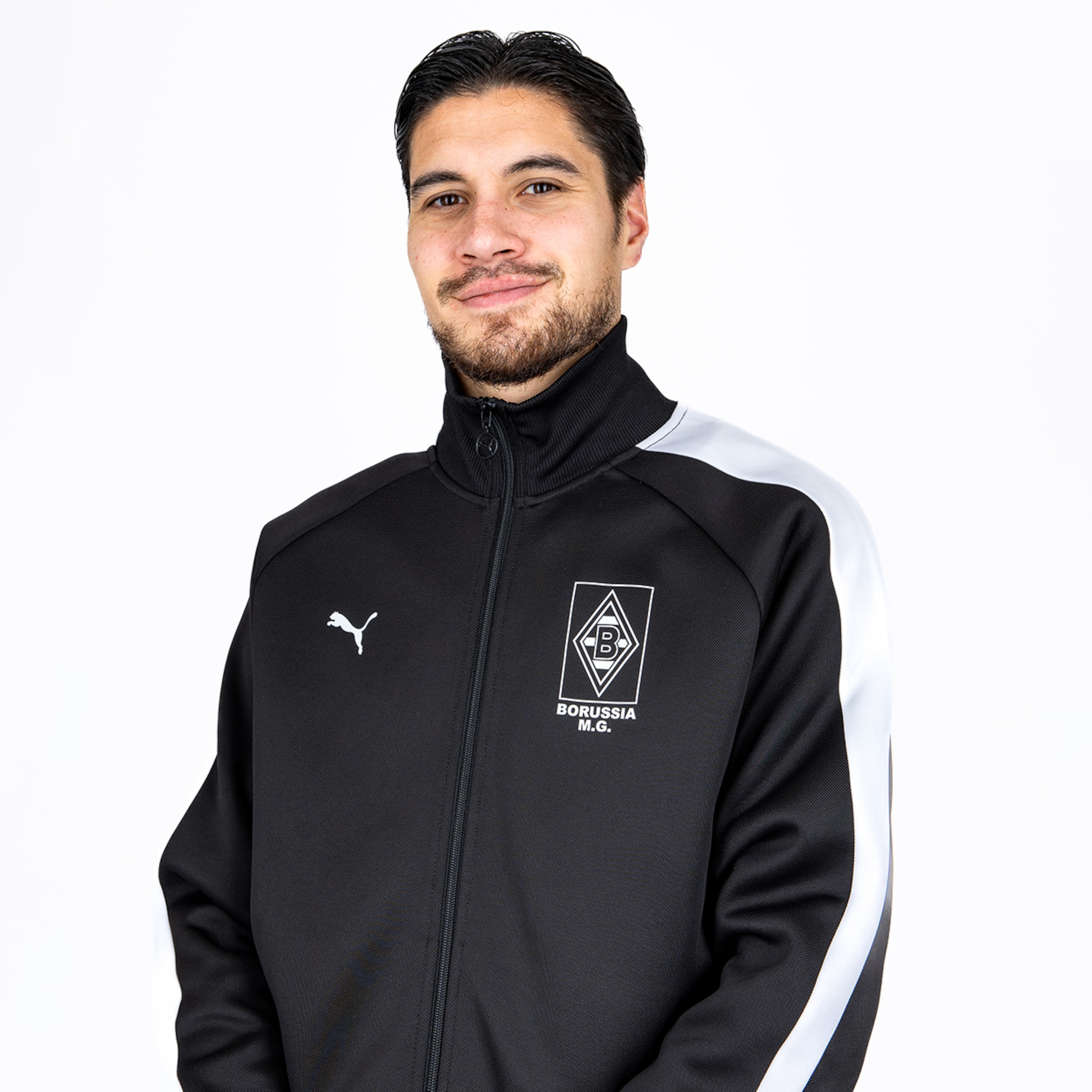 Porträt eines lächelnden Mannes mit Bart in einer schwarzen Puma-Trainingsjacke von Borussia Mönchengladbach vor weißem Hintergrund.