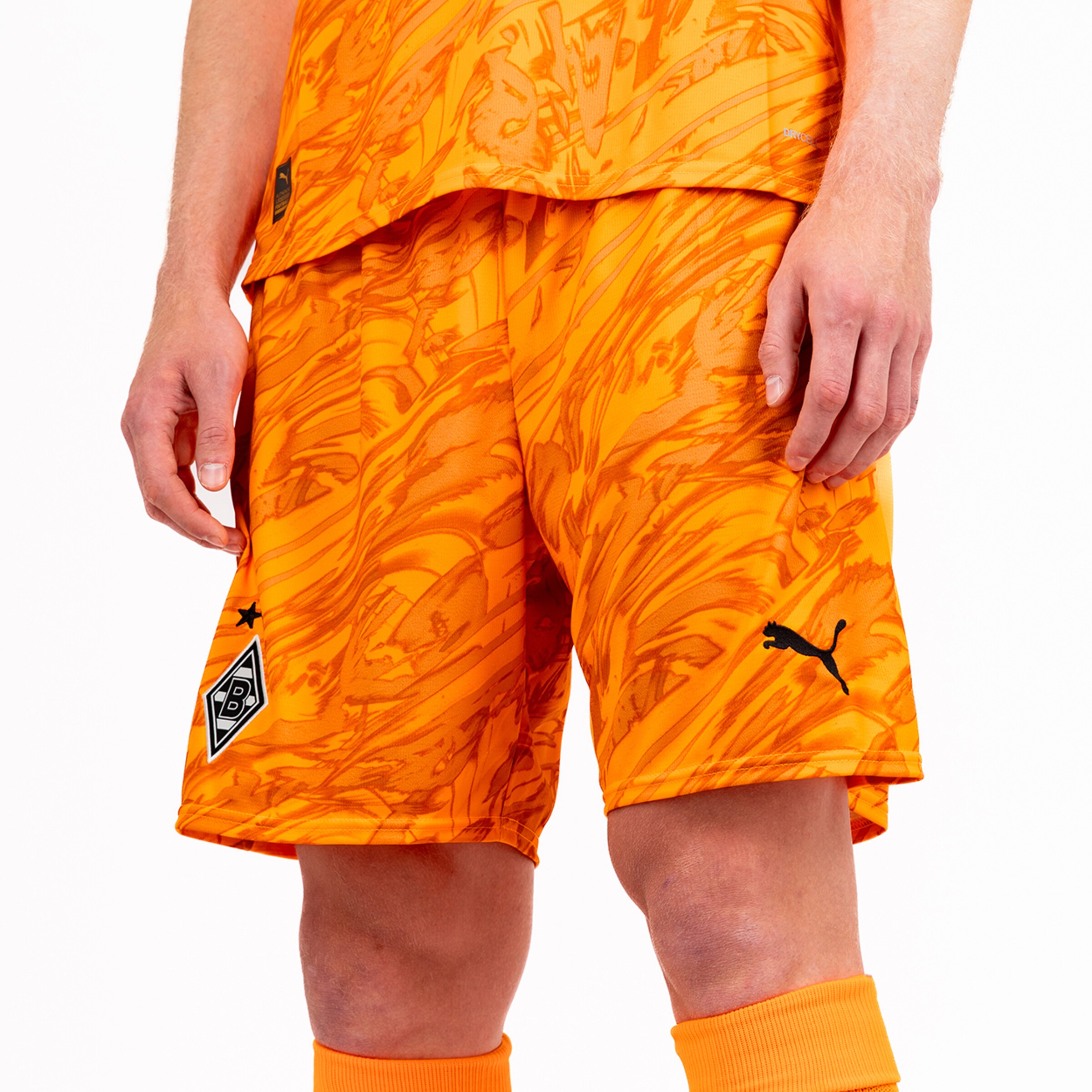 Shorts made of orange material with an abstract pattern and a Puma logo worn by a person.