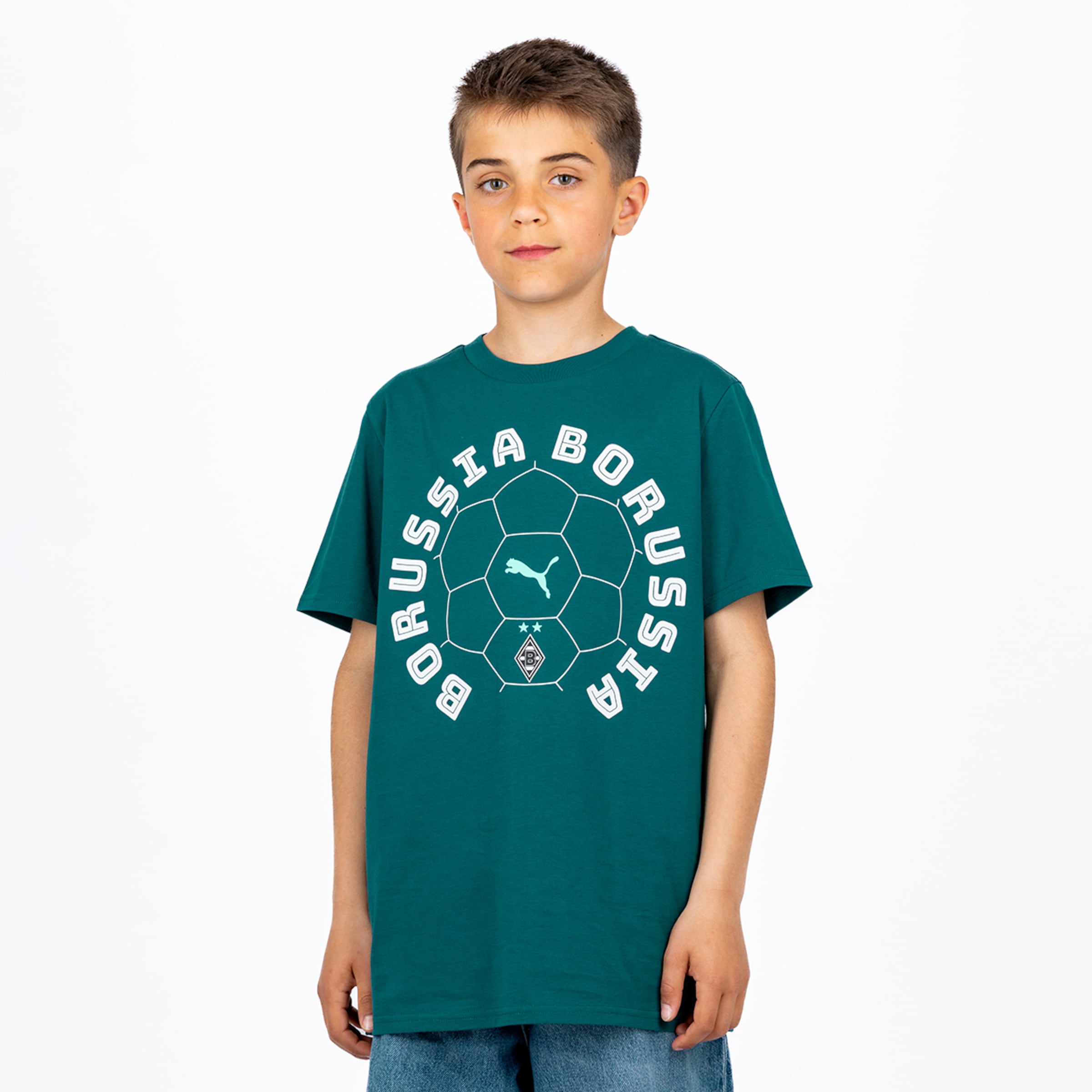 Ein Junge in einem petrolfarbenen „BORUSSIA“-Fußball-T-Shirt mit Puma- und Borussia Mönchengladbach-Logos und blauen Jeans, steht vor weißem Hintergrund und blickt in die Kamera.