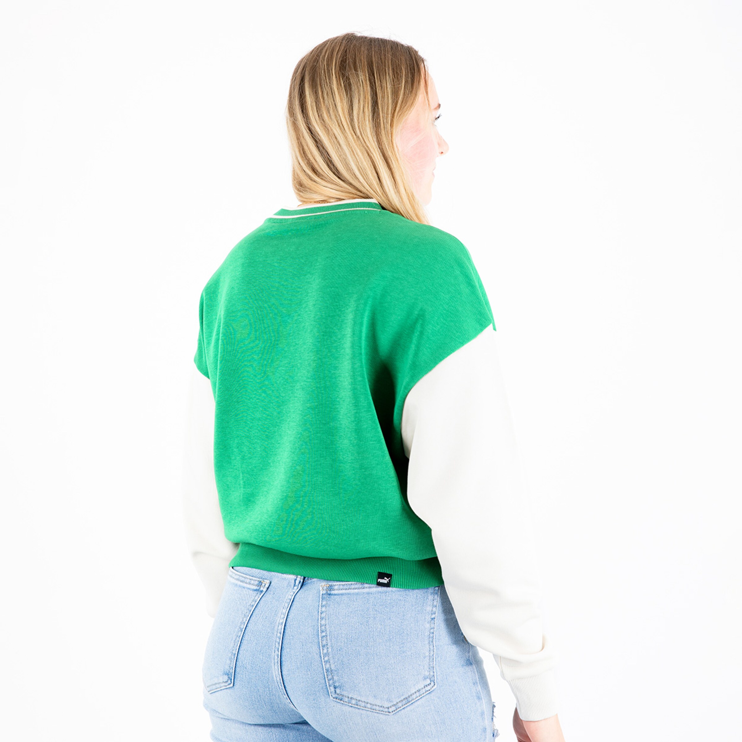 Frau steht mit dem Rücken zu trägt einen grünen Pullover mit weißen Ärmeln und Jeans.