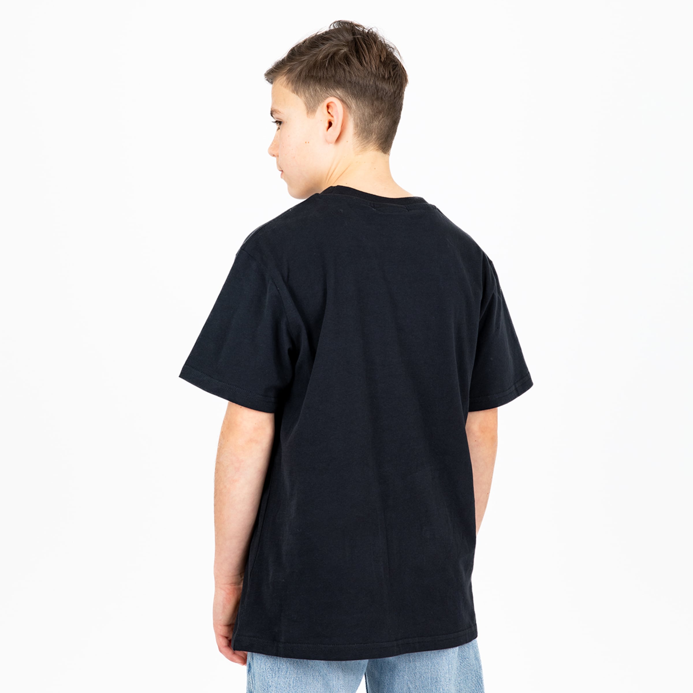 Junge steht mit dem Rücken zur Kamera trägt ein schwarzes T-Shirt und hellblaue Jeans.