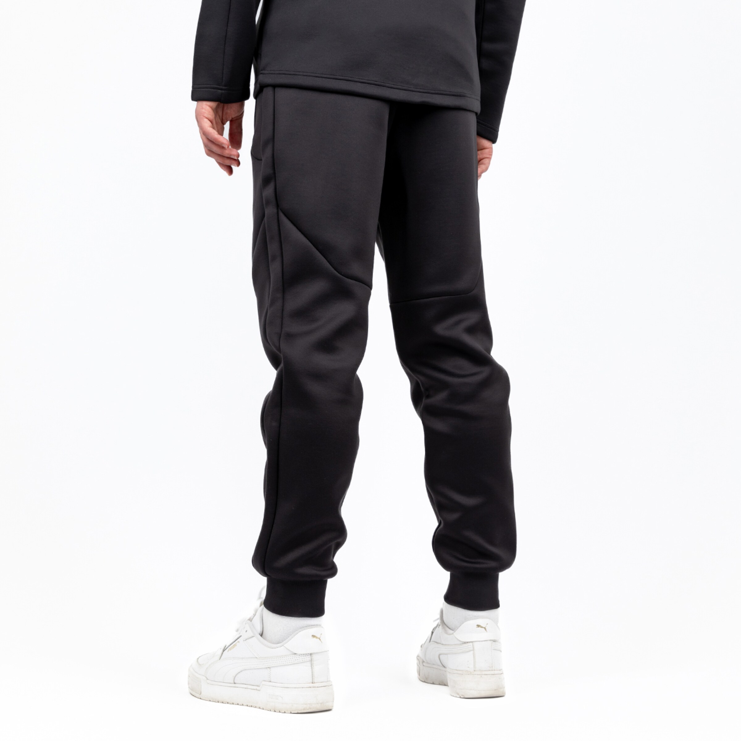 Eine Person trägt schwarze Sporthose und weiße Sneakers Blick von hinten.