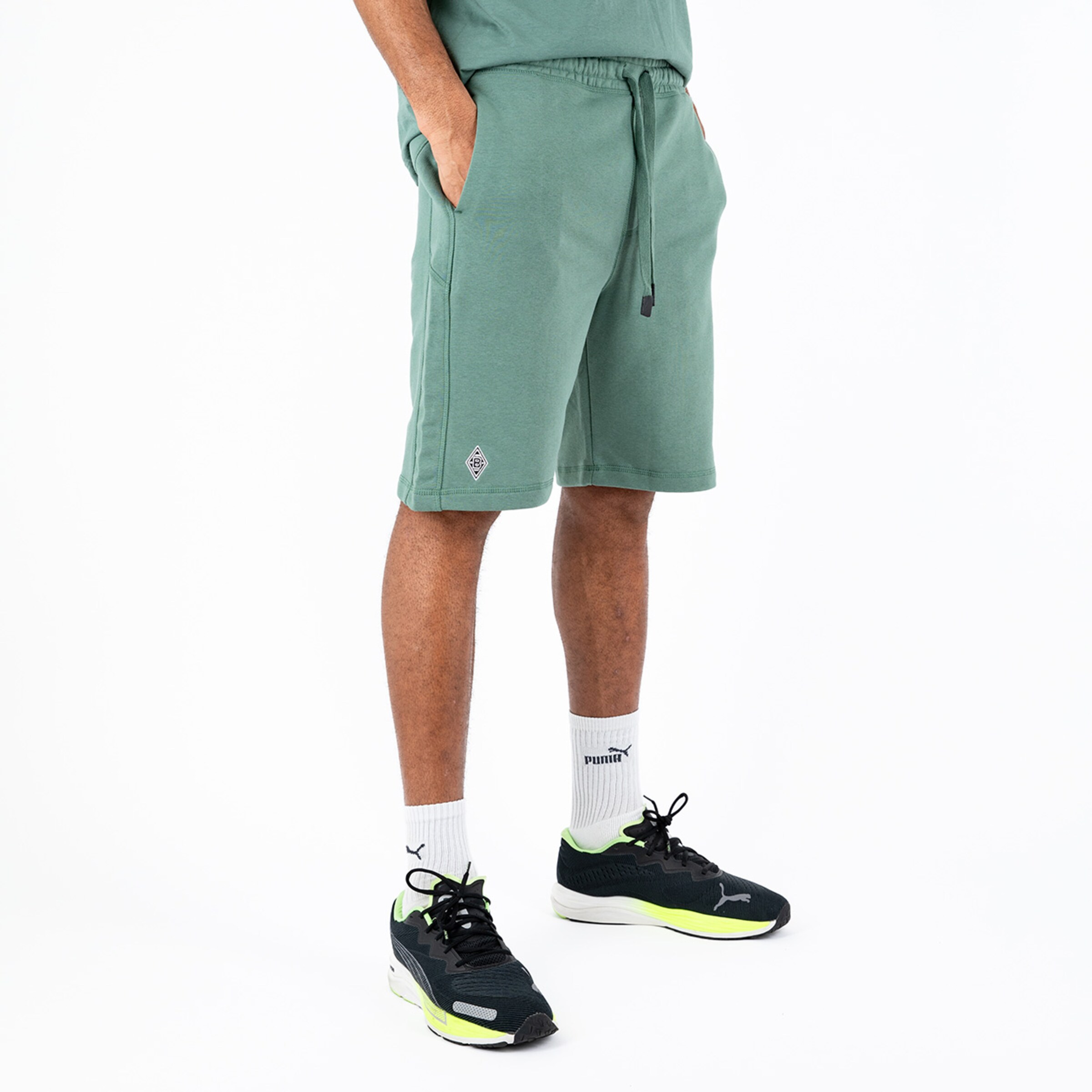 Herren in grünem Sportshort mit Taschen und verstellbarem Bund kombiniert mit Sneakers.