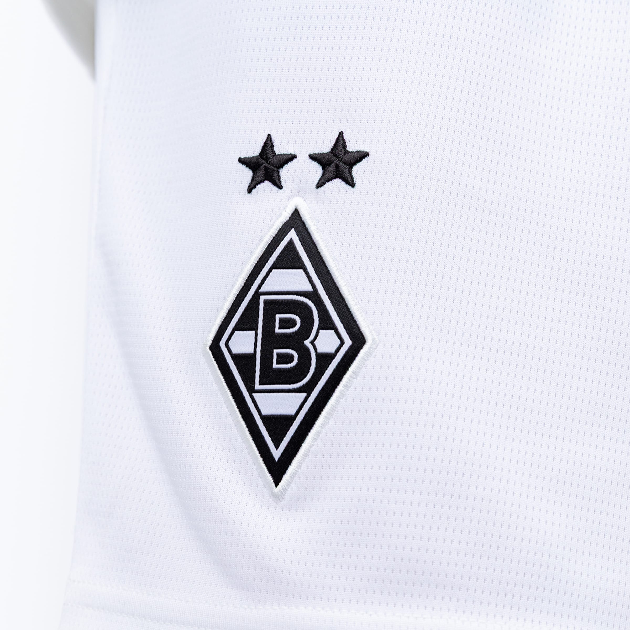 Gesticktes Logo von Borussia Mönchengladbach auf weißem Stoff: Schwarze Raute mit weißem „B“ und zwei schwarzen Sternen darüber.