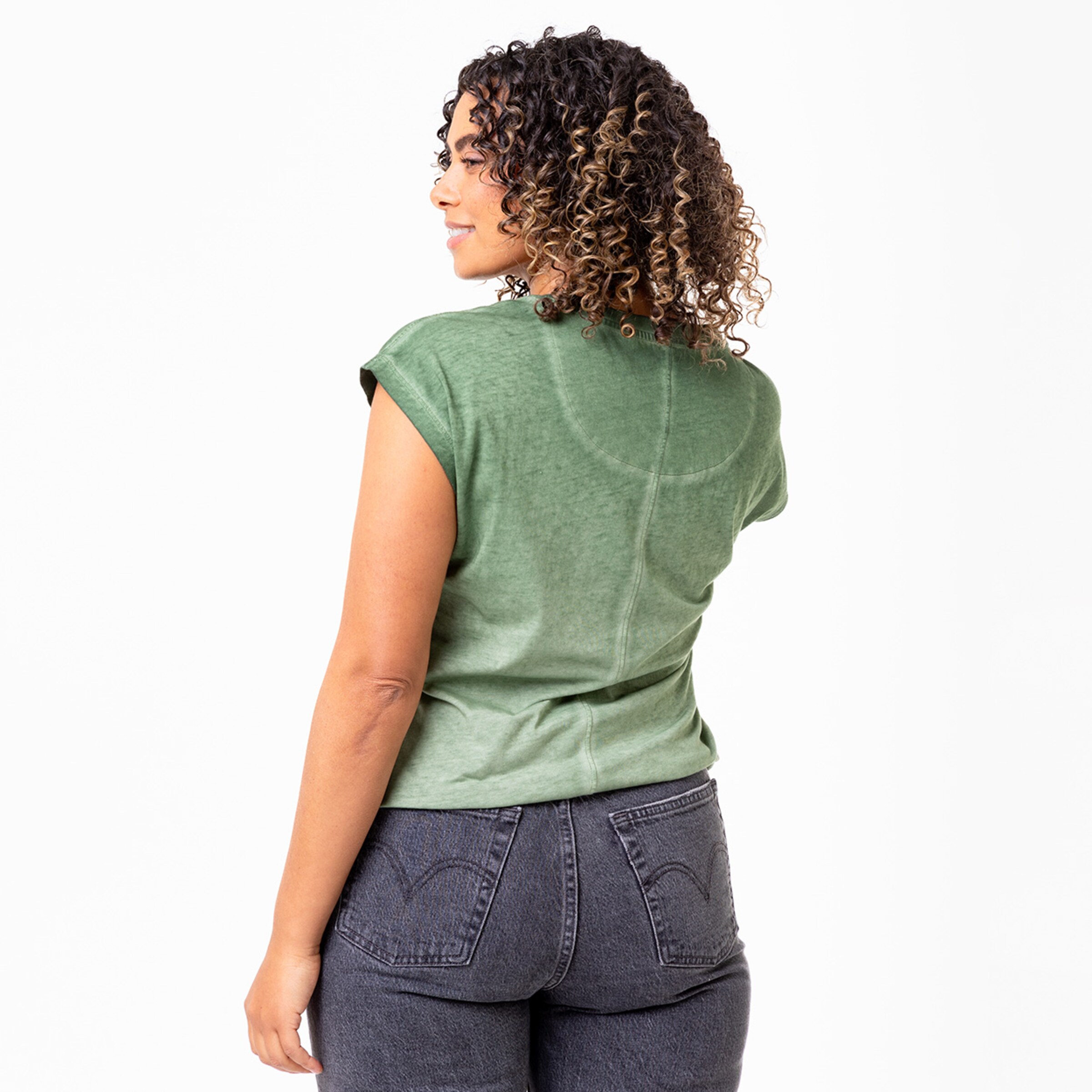 Dame mit lockigem Haar trägt ein grünes Oberteil und schaut über die Schulter zurück.