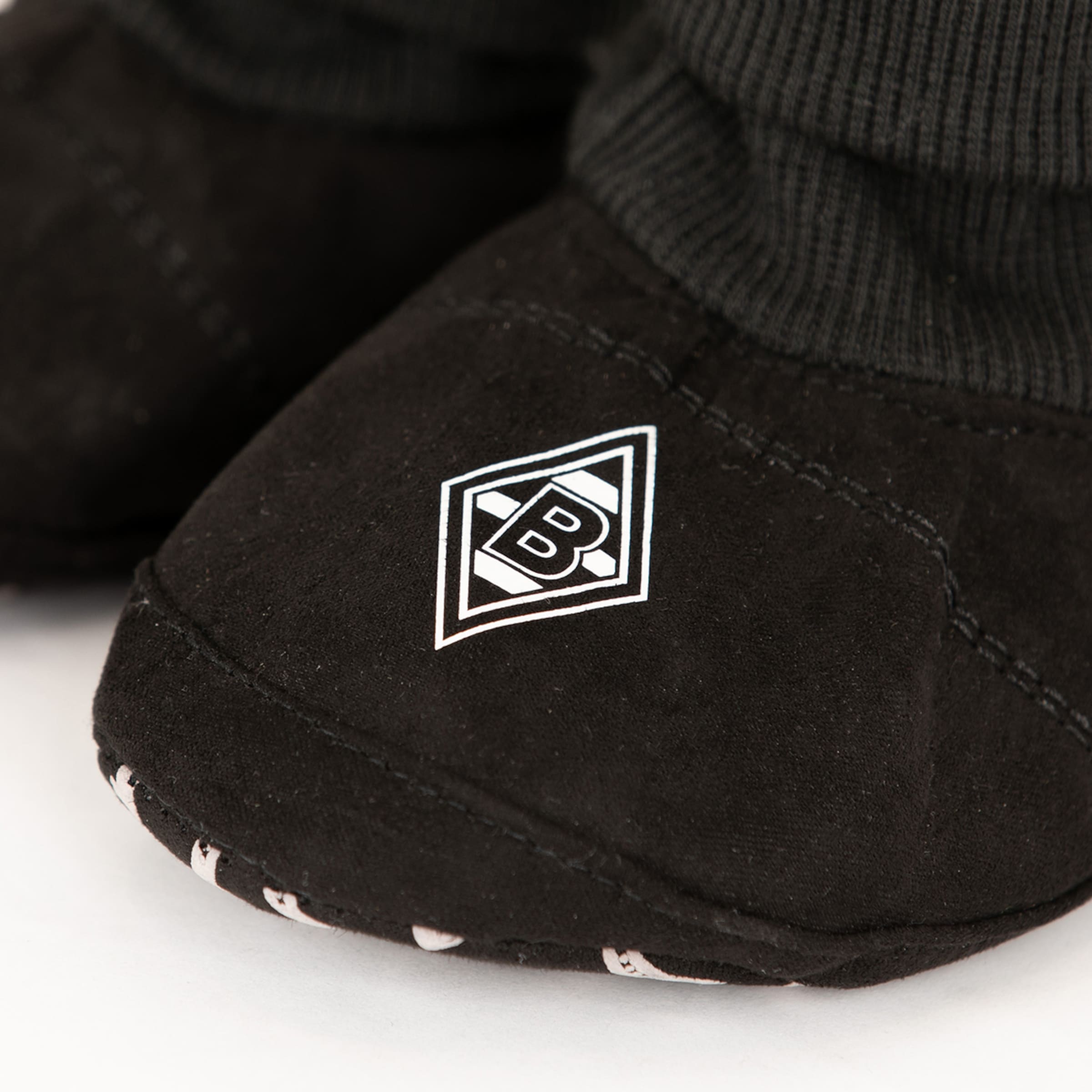 Schwarzer Babyschuh in Wildlederoptik mit dem Logo von Borussia Mönchengladbach auf der Vorderseite.