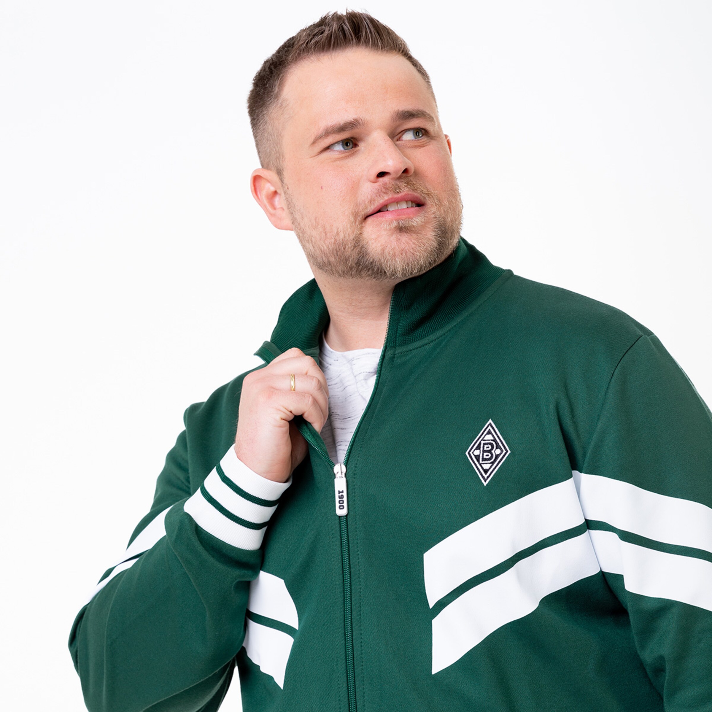 Ein Mann trägt eine grüne Trainingsjacke mit weißen Streifen und dem Borussia Mönchengladbach-Logo.