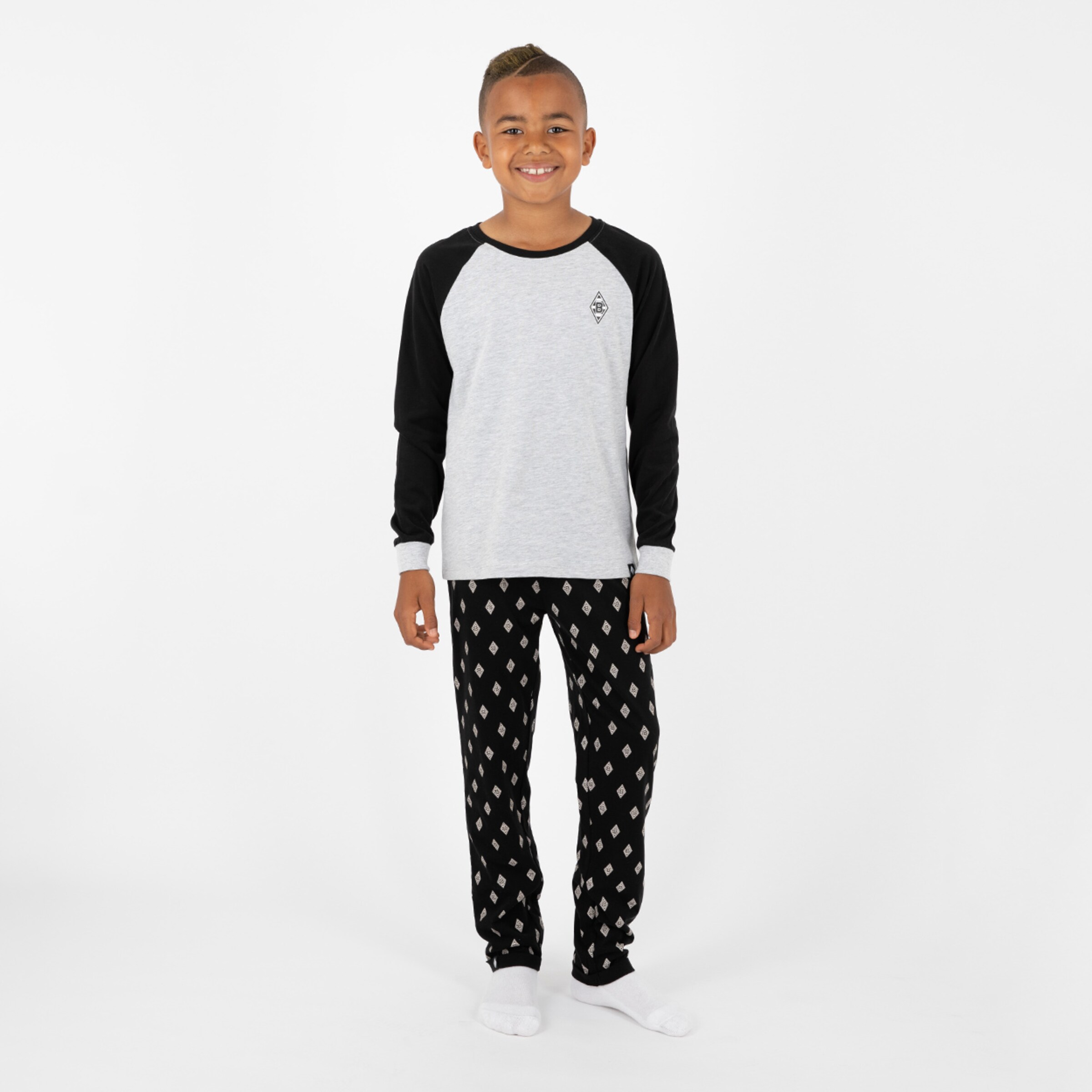 Ein Junge trägt ein graues Oberteil mit schwarzen Ärmeln und schwarze Pyjamahosen mit einem Muster.