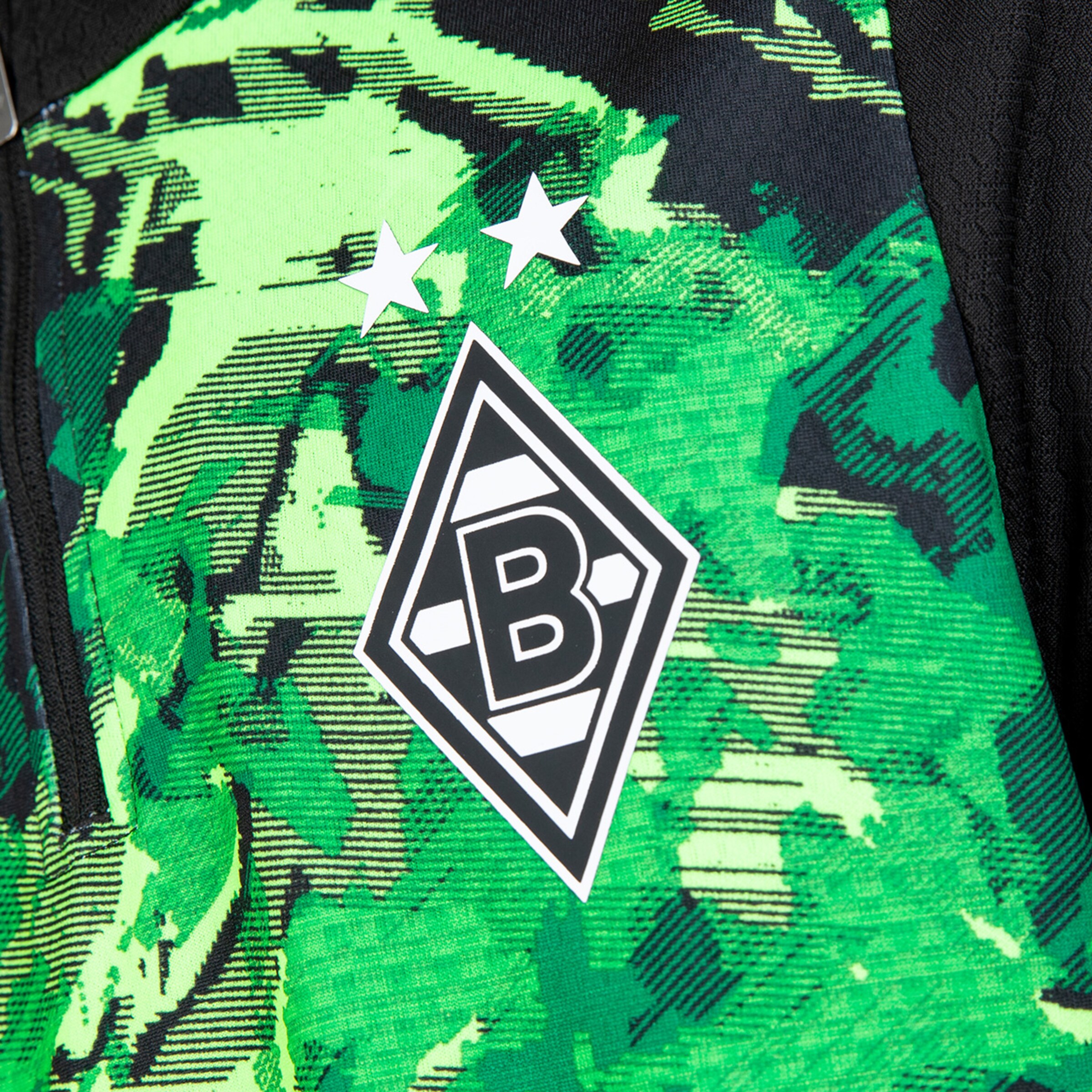 Detailaufnahme des Borussia Mönchengladbach Logos auf einem grün gemusterten Trikot.