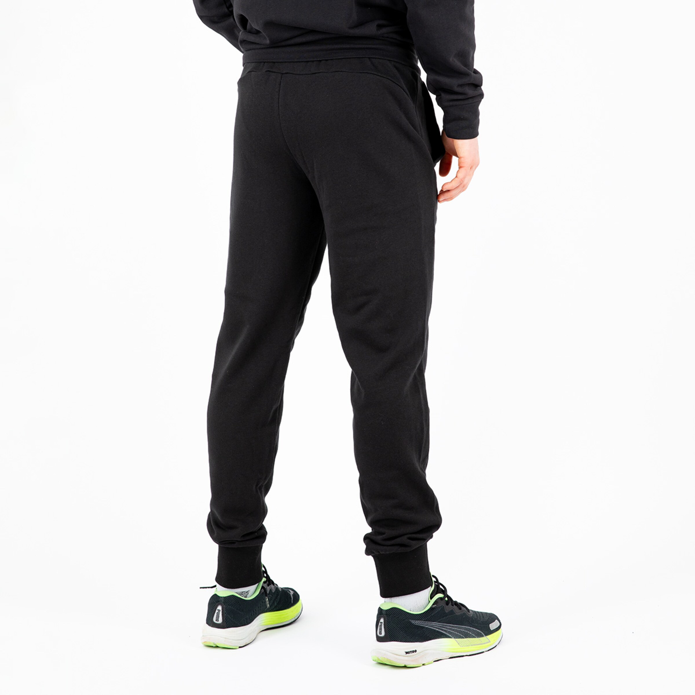 Person von hinten in schwarzen Jogginghosen und Sportschuhen die auf einer weißen Fläche steht.