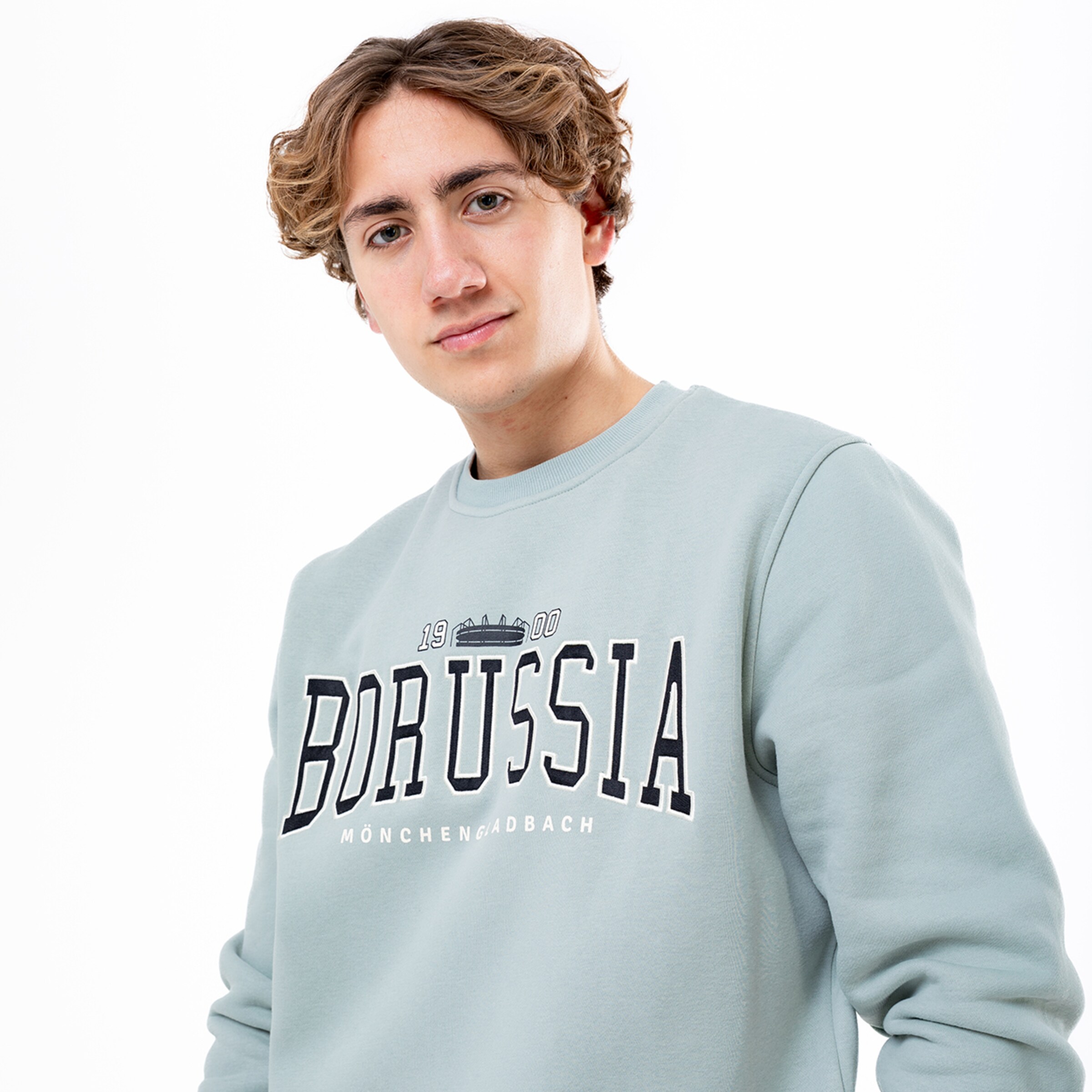 Ein junger Mann trägt einen hellblauen Sweatshirt mit dem Schriftzug BORUSSIA MÖNCHENGLADBACH.
