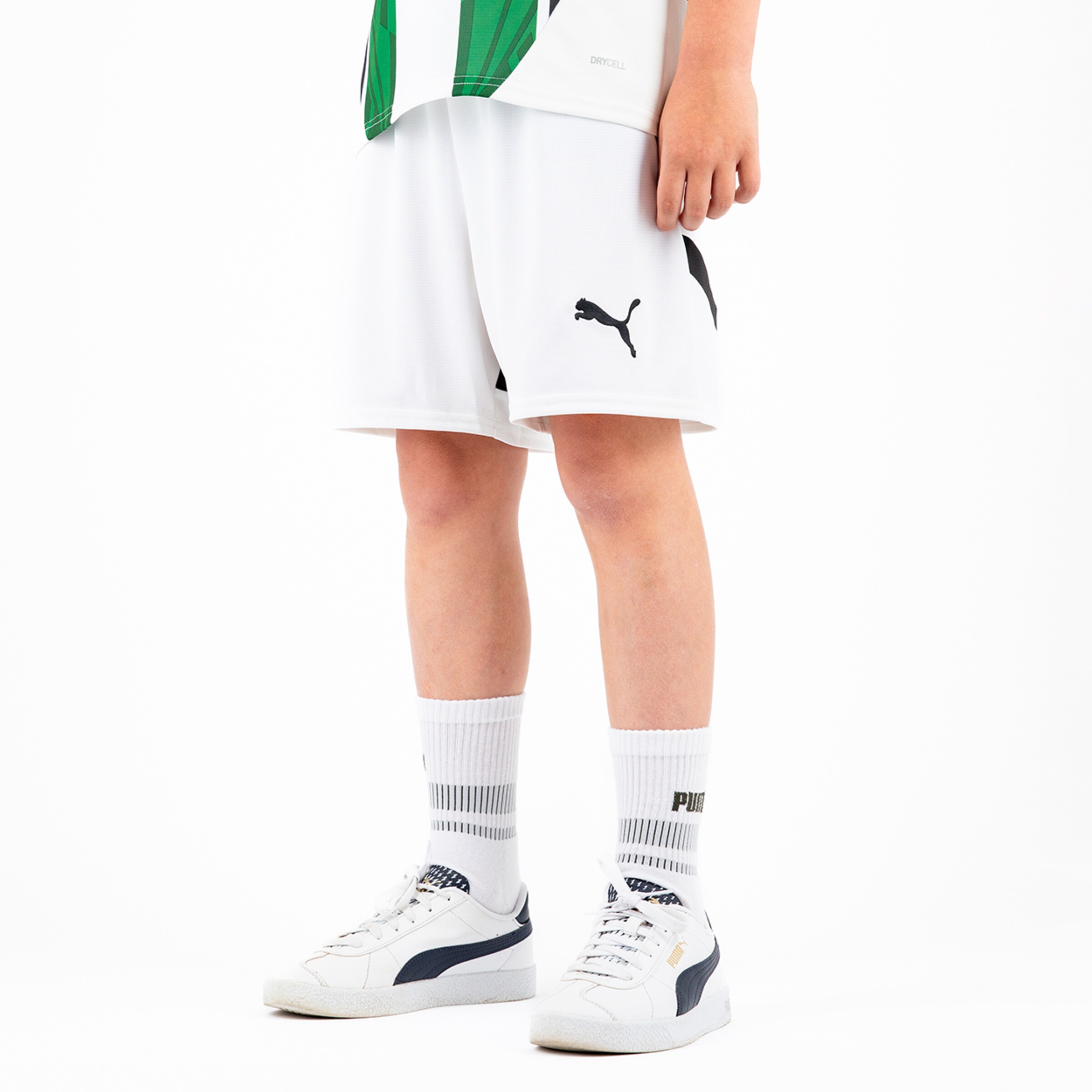 A boy is wearing a Borussia Mönchengladbach soccer jersey white shorts and white sneakers.