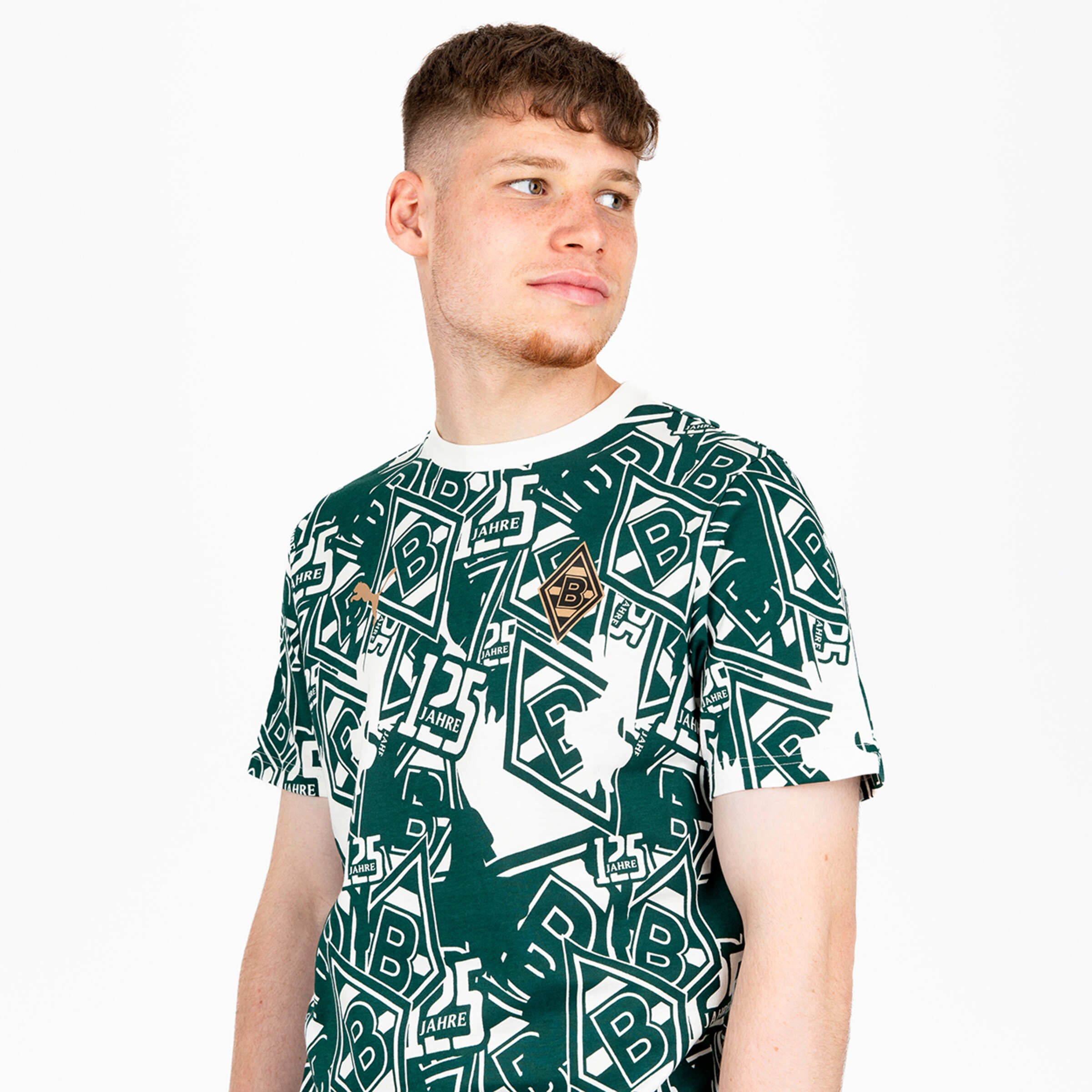 Junger Mann in einem grün-weißen Borussia Mönchengladbach T-Shirt mit Logo-Print und „125 Jahre“ Schriftzug vor weißem Hintergrund.