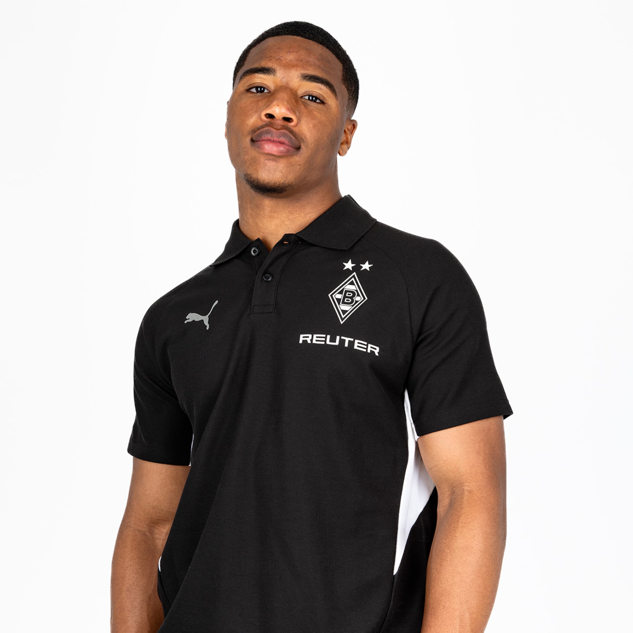 Ein junger Mann posaunt in einem schwarzen Poloshirt mit Puma-Logo und Borussia Mönchengladbach-Wappen.